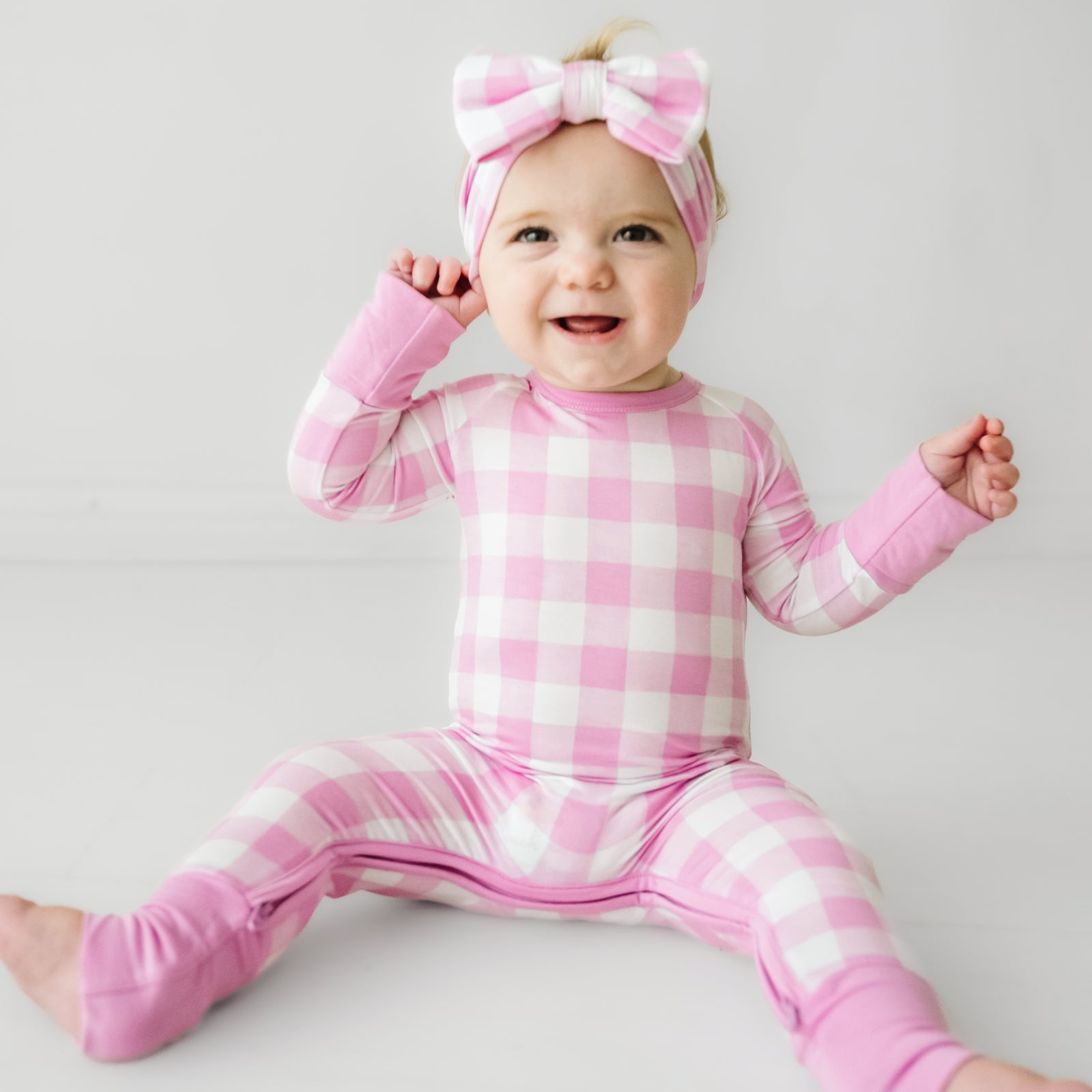 Child wearing a Pink Gingham crescent zippy paired with a matching luxe bow headband