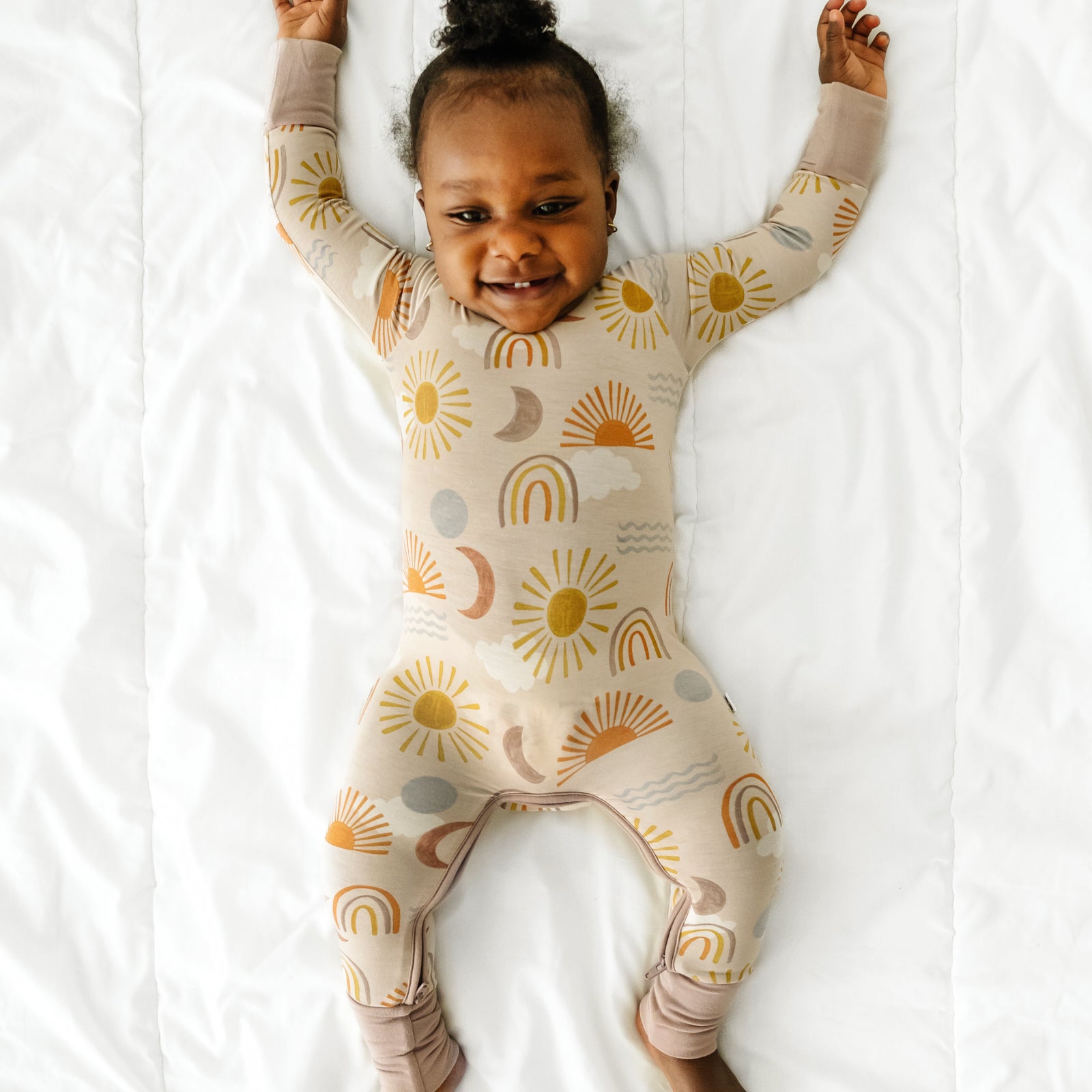 Child stretching on a bed wearing a Desert Sunrise crescent zippy