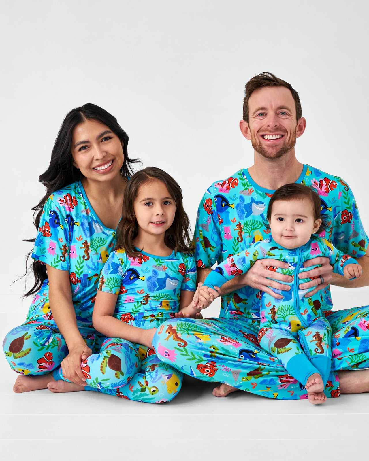 Sitting family of four wearing matching Nemo's Reef bamboo pajamas