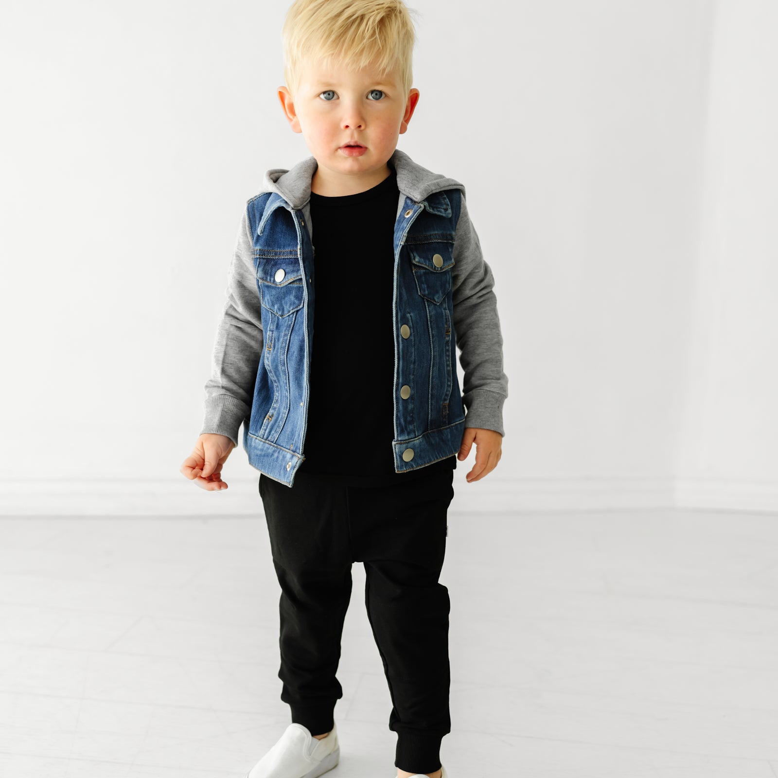 Boy wearing a denim jacket with gray sleeves and black leggings.