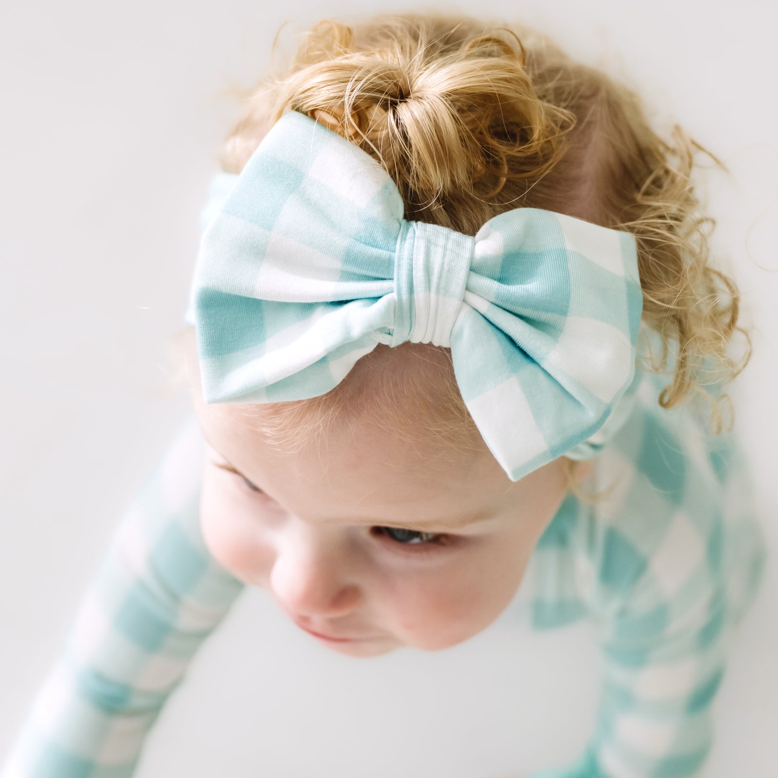 Close up image of a child wearing an Aqua Gingham luxe bow headband
