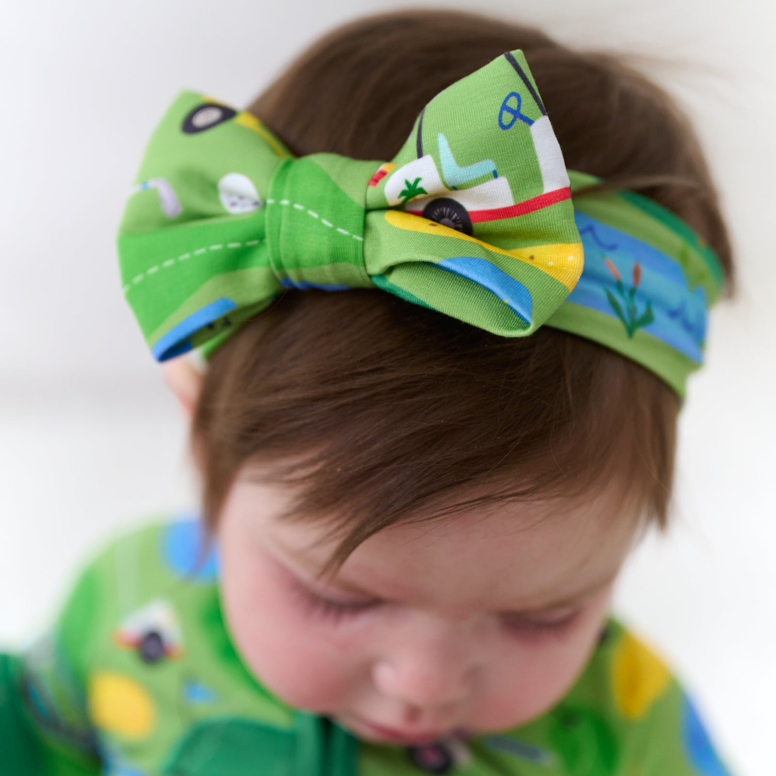 Close up image of a child wearing a Fairway Fun luxe bow headband and matching zippy