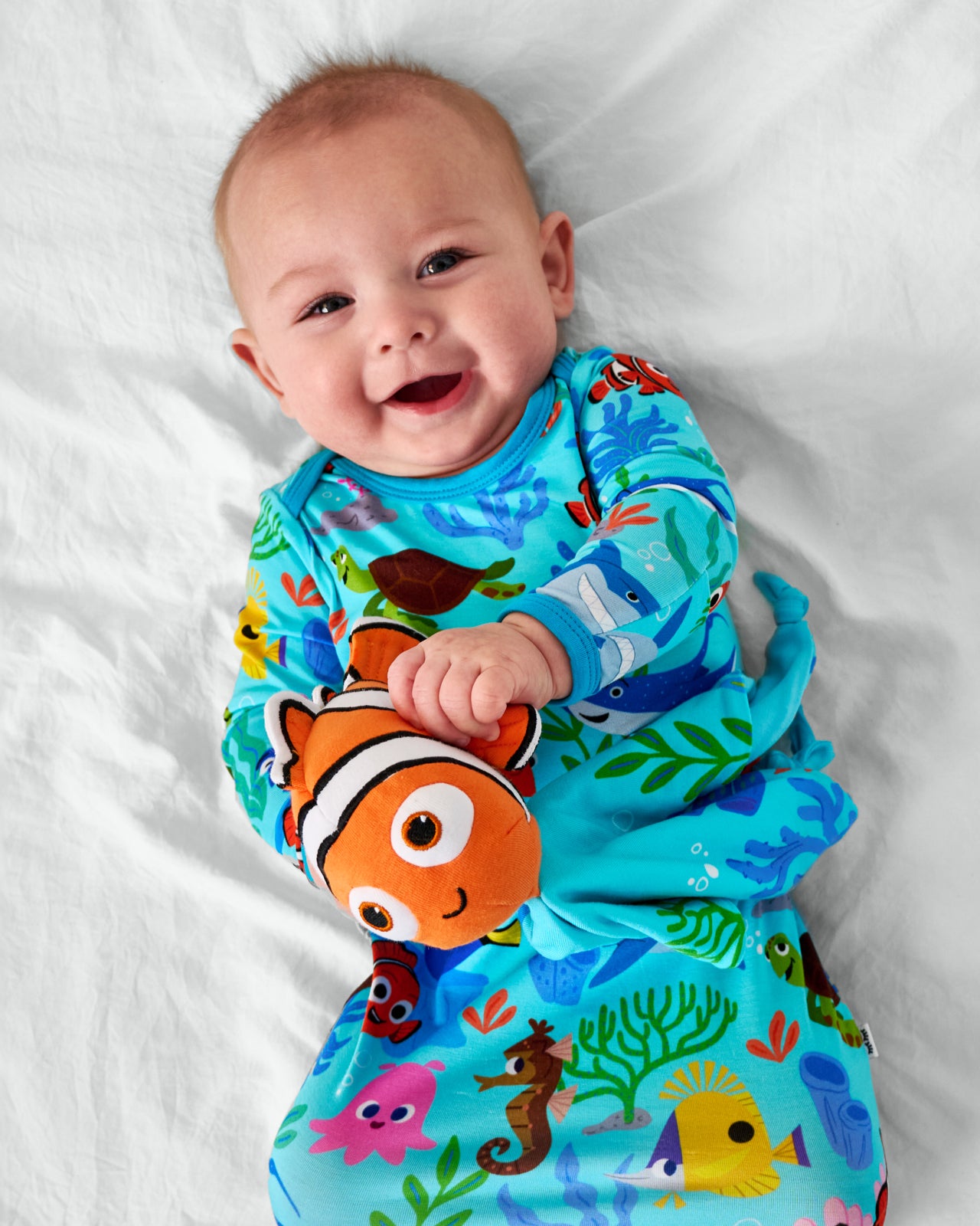 Baby wearing the Nemo's Reef Infant Gown holding the Disney Nemo Lovey