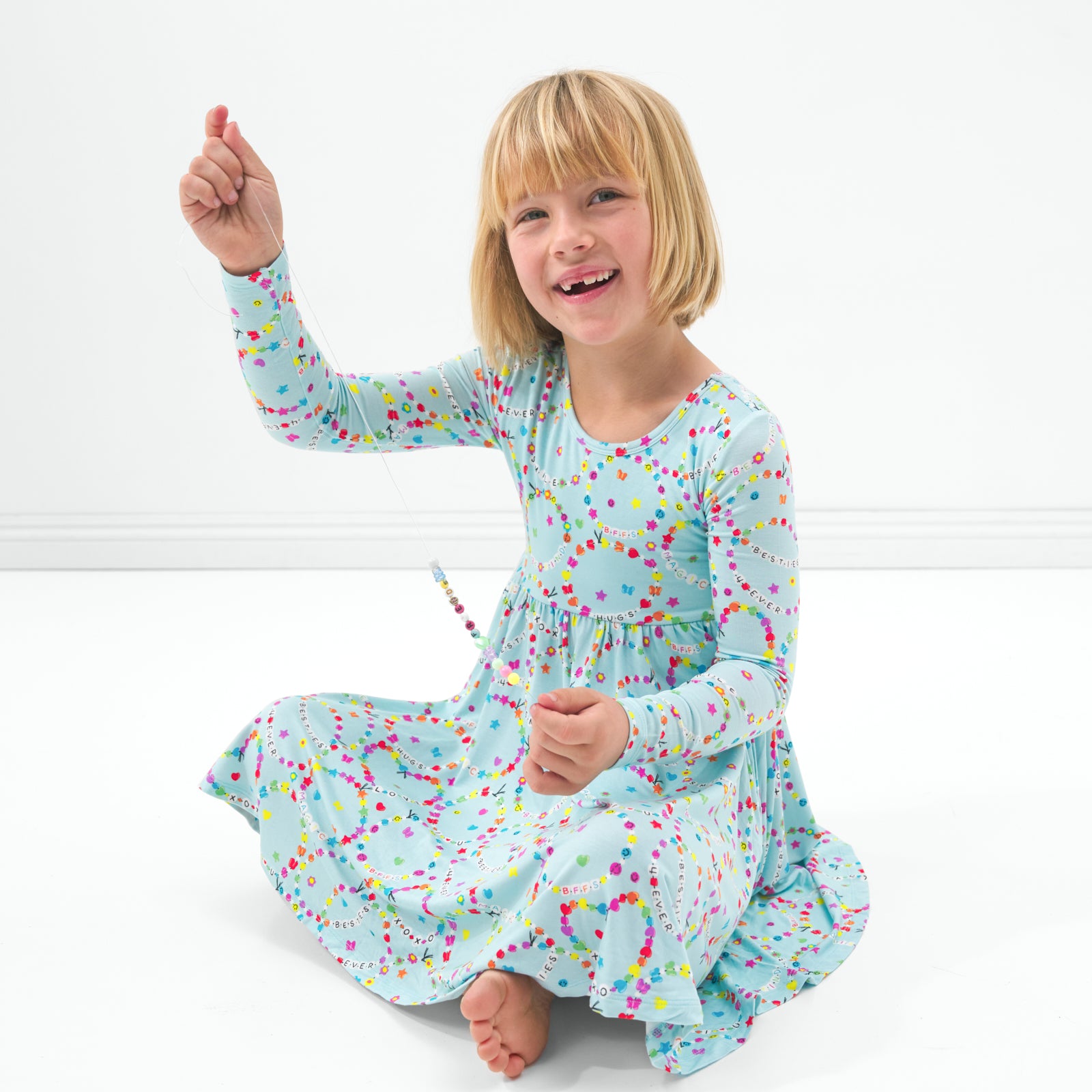 Sitting child wearing the Friends Forever twirl dress holding up a beaded friendship bracelets