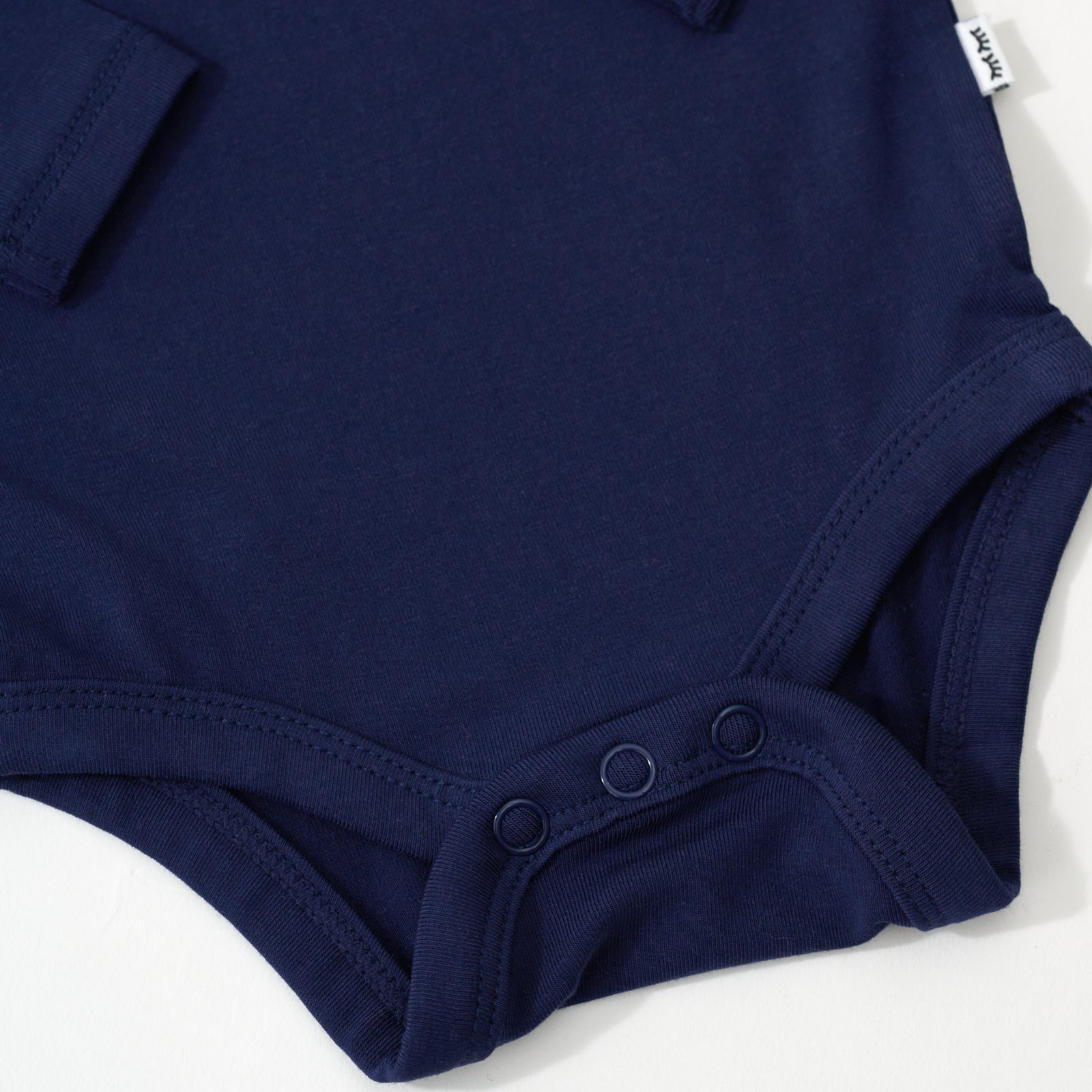 Close up flat lay image of the snap detail on the Classic Navy Long Sleeve Bodysuit