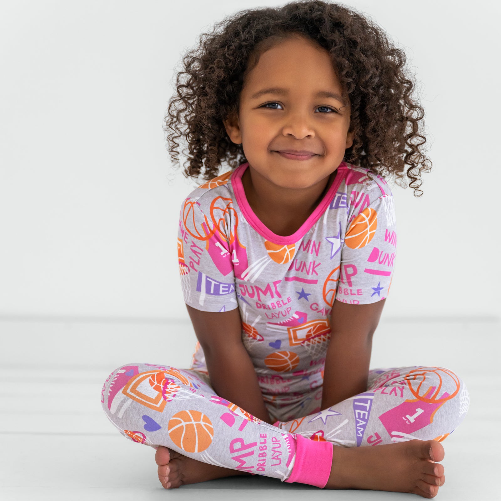 Sitting child wearing the Pink Slam Dunk short sleeve bamboo pajama set