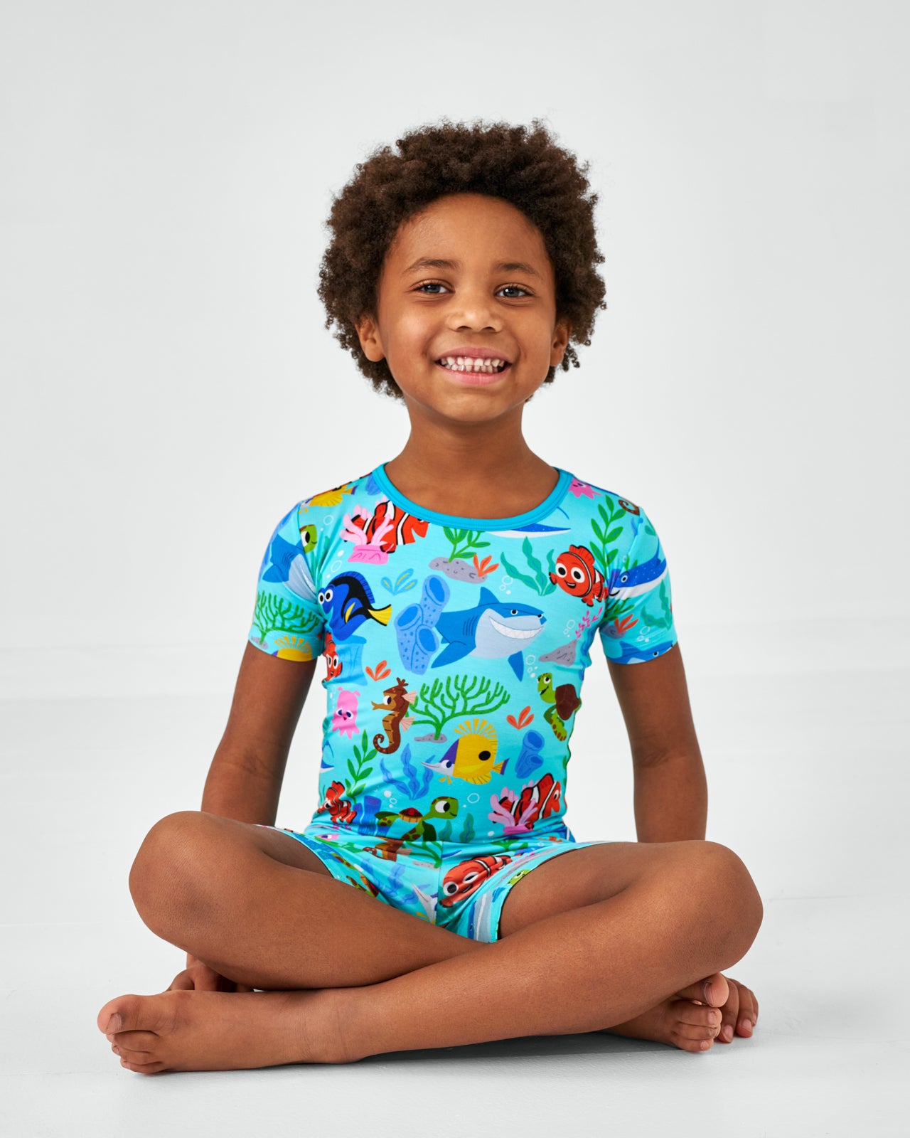 Sitting child wearing the Disney Nemo's Reef Two-Piece Short Sleeve & Shorts bamboo Pajama Set