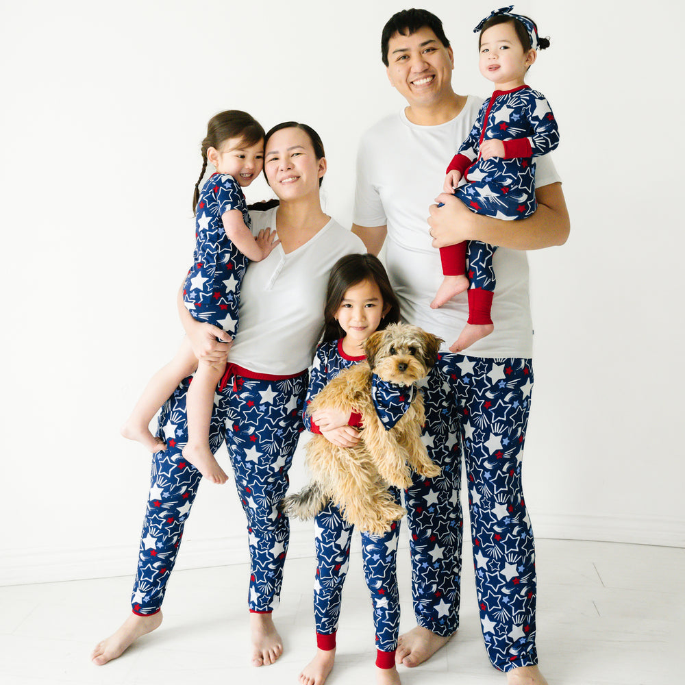Family of five wearing matching Star Spangled pajamas. Dad is wearing men's bright white pj top with men's Star Spangled pj pants. Mom is wearing a women's bright white pj top with women's Star Spangled pj pants. Their kids are wearing Star Spangled printed pjs in two piece and zippy styles. Their dog is wearing a matching pet bandana