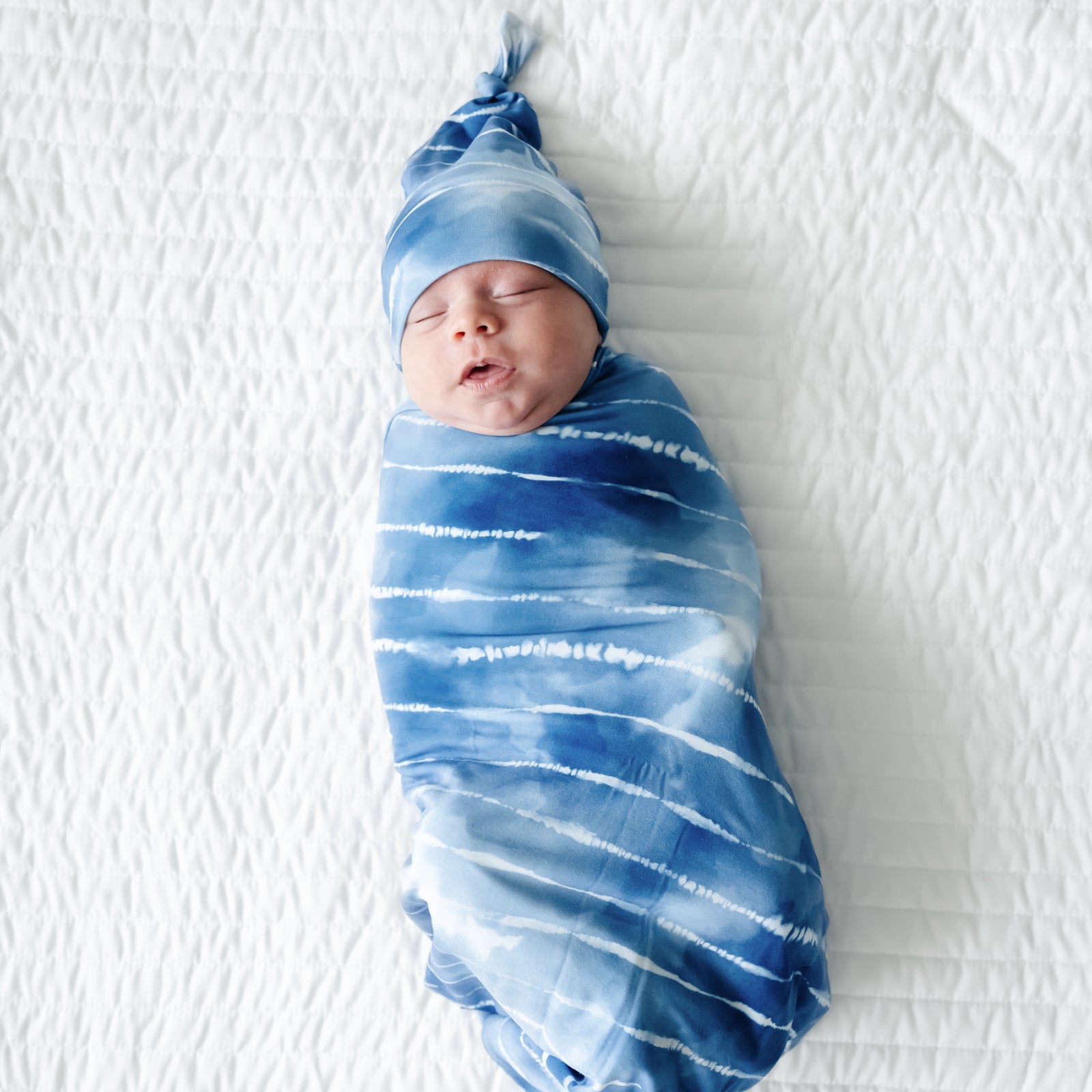 Infant swaddled in a Blue Tie Dye Dreams swaddle & hat set