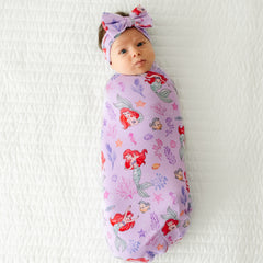 Child swaddled in a Disney Part of Her World swaddle and luxe bow headband set