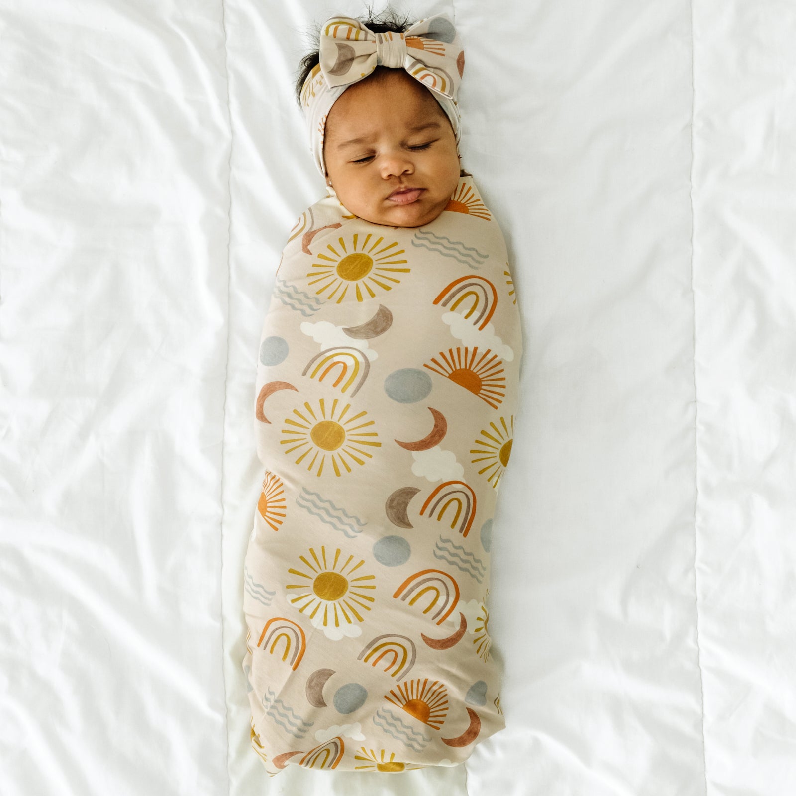 Child swaddled in a Desert Sunrise swaddle & luxe bow headband set
