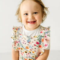 Close up image of a child wearing a Mauve Meadow ruffle overall and coordinating Play top