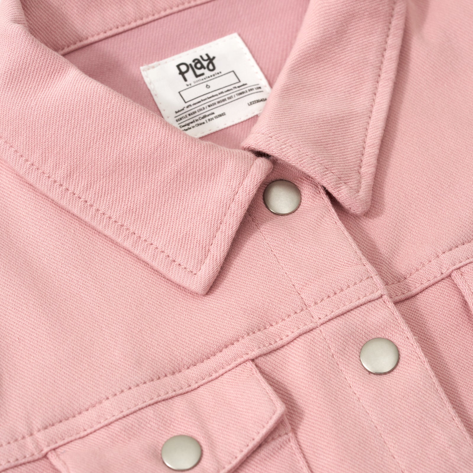 Close up image of the buttoned collar and pockets on the Mauve Blush Denim Trucker Jacket