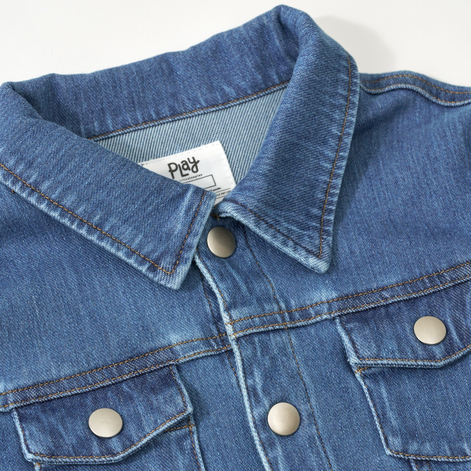 Close up flat lay image of buttoned collar and chest pocket detail on the Midwash Blue Denim Trucker Jacket