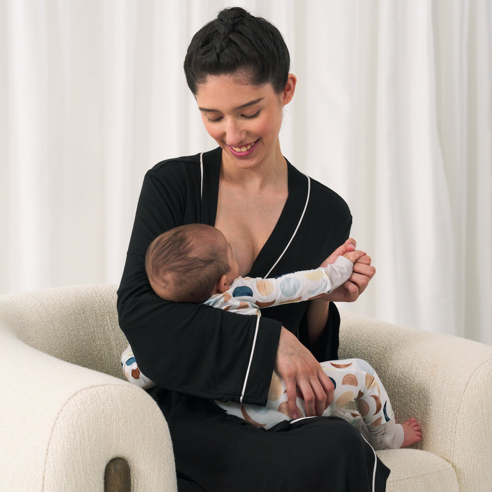 woman nursing her child wearing a women's black robe. Her child is wearing a luna neutral zippy