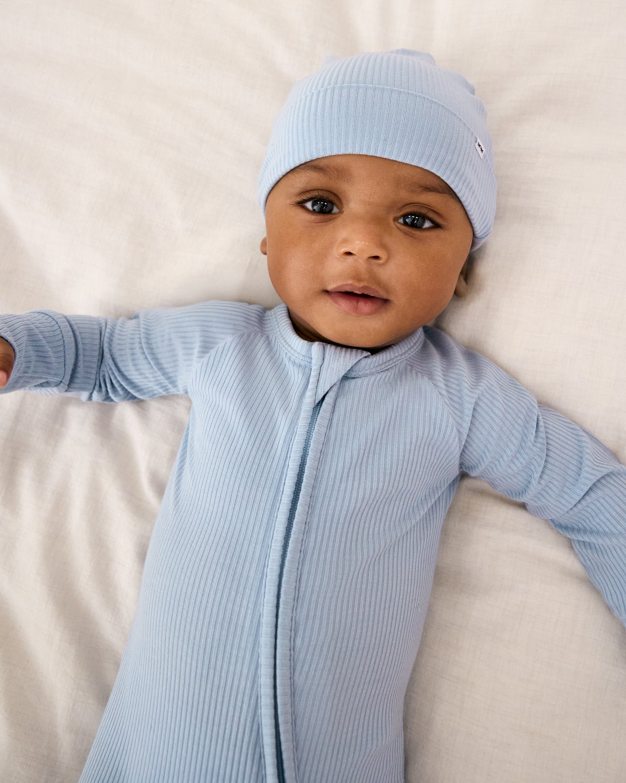 Aerial view of baby wearing the Light Fog Newborn Ribbed Zippy with a matching infant beanie