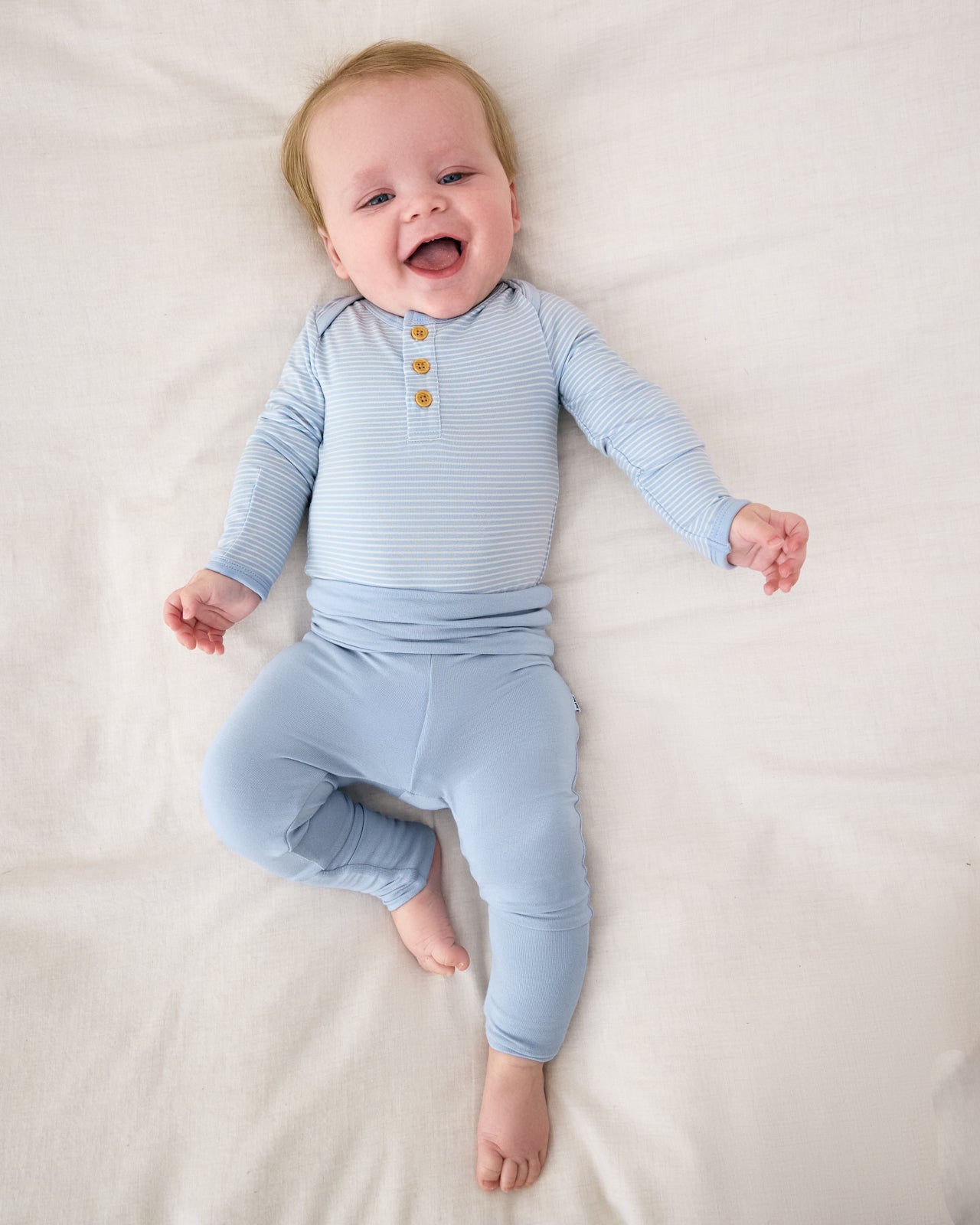 Aerial view of baby wearing the Light Fog Stripe Henley Bodysuit with matching blue newborn leggings