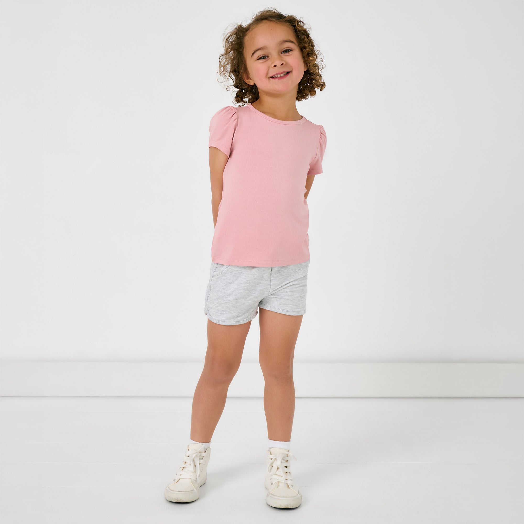 Standing girl wearing the Light Heather Gray Dolphin Shorts and a pink puff sleeve tee