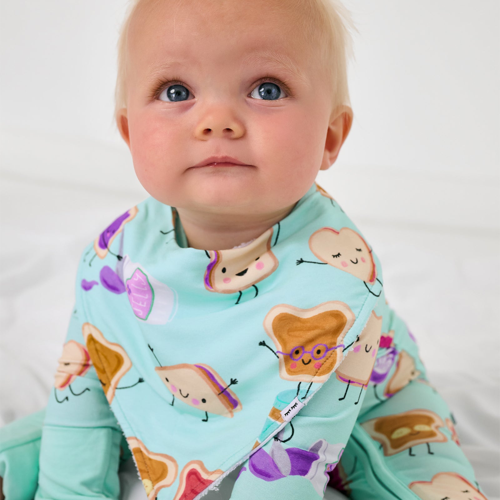 Sitting baby wearing the Lunch Buddies Bandana Bib and matching zipper pajamas