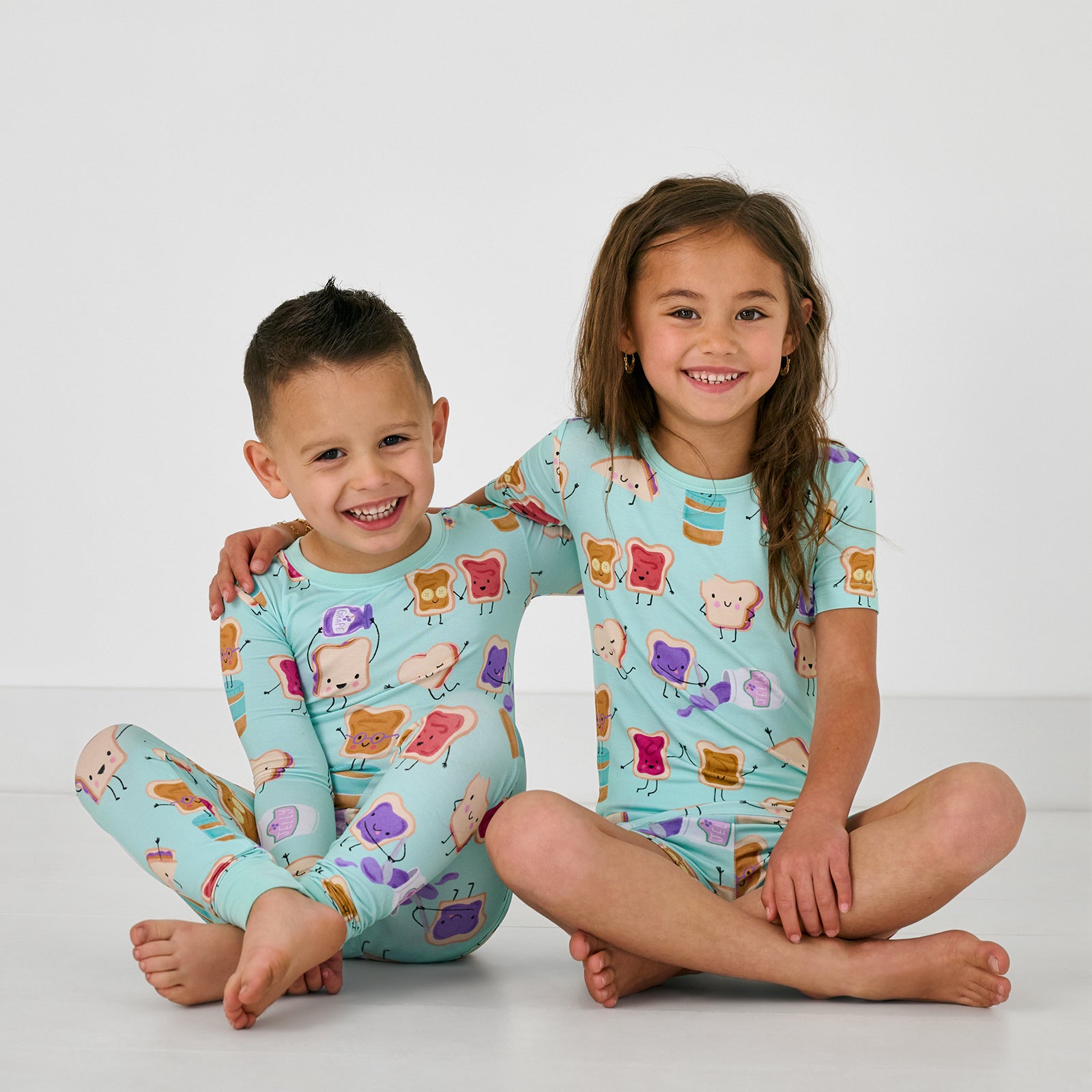 Two sitting children wearing matching Lunch Buddies Two-Piece bamboo kids pajamas