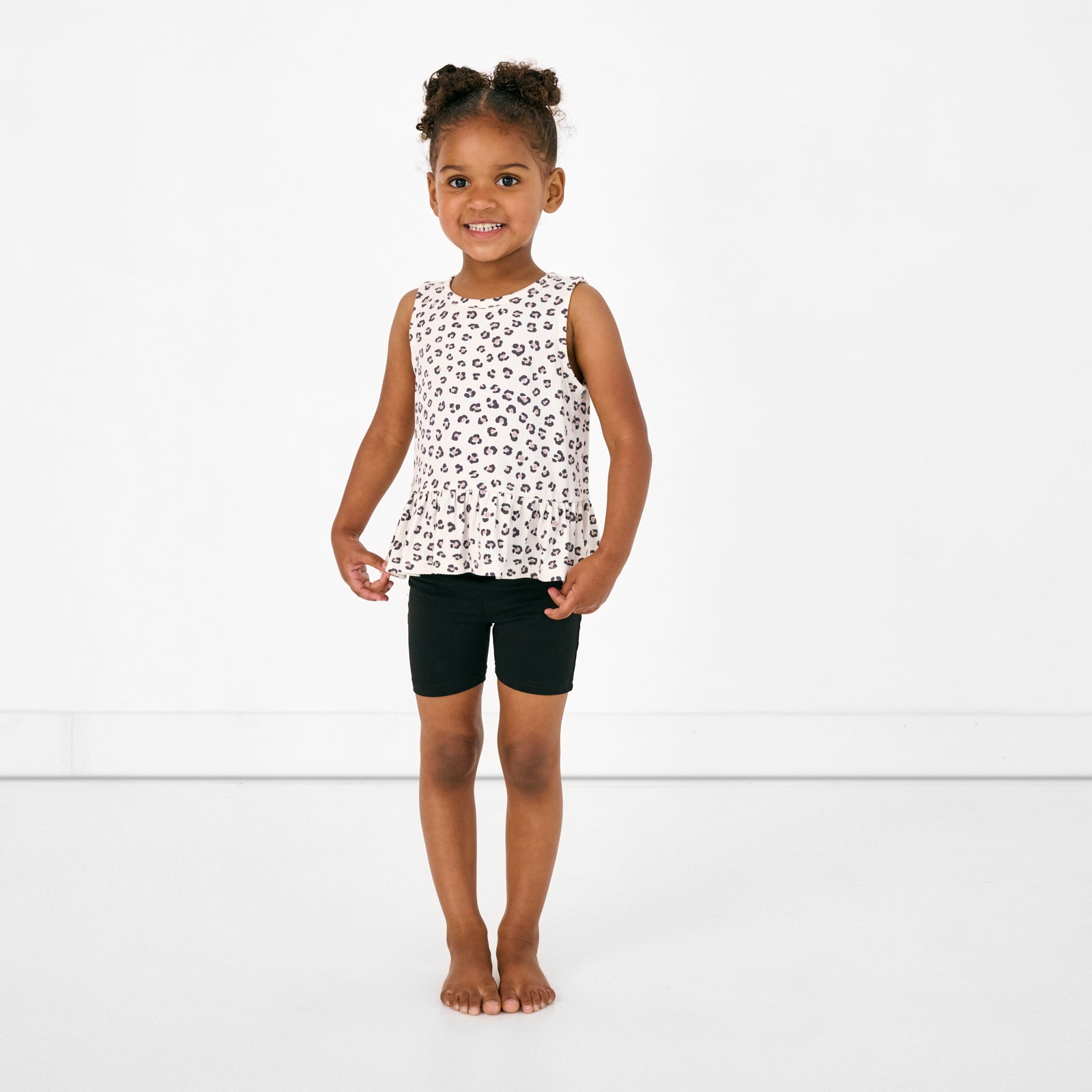 Standing child wearing the Luxe Leopard Peplum Tank with black bike shorts