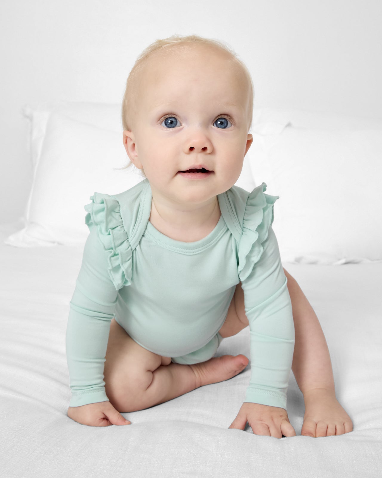 Baby wearing the Mint Mist Flutter Bodysuit on a white bed