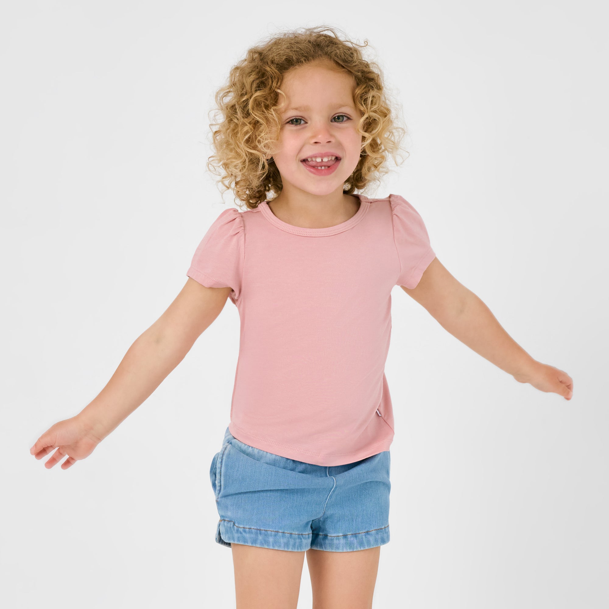 Posing child wearing the Mauve Blush Puff Sleeve Tee with blue denim shorts