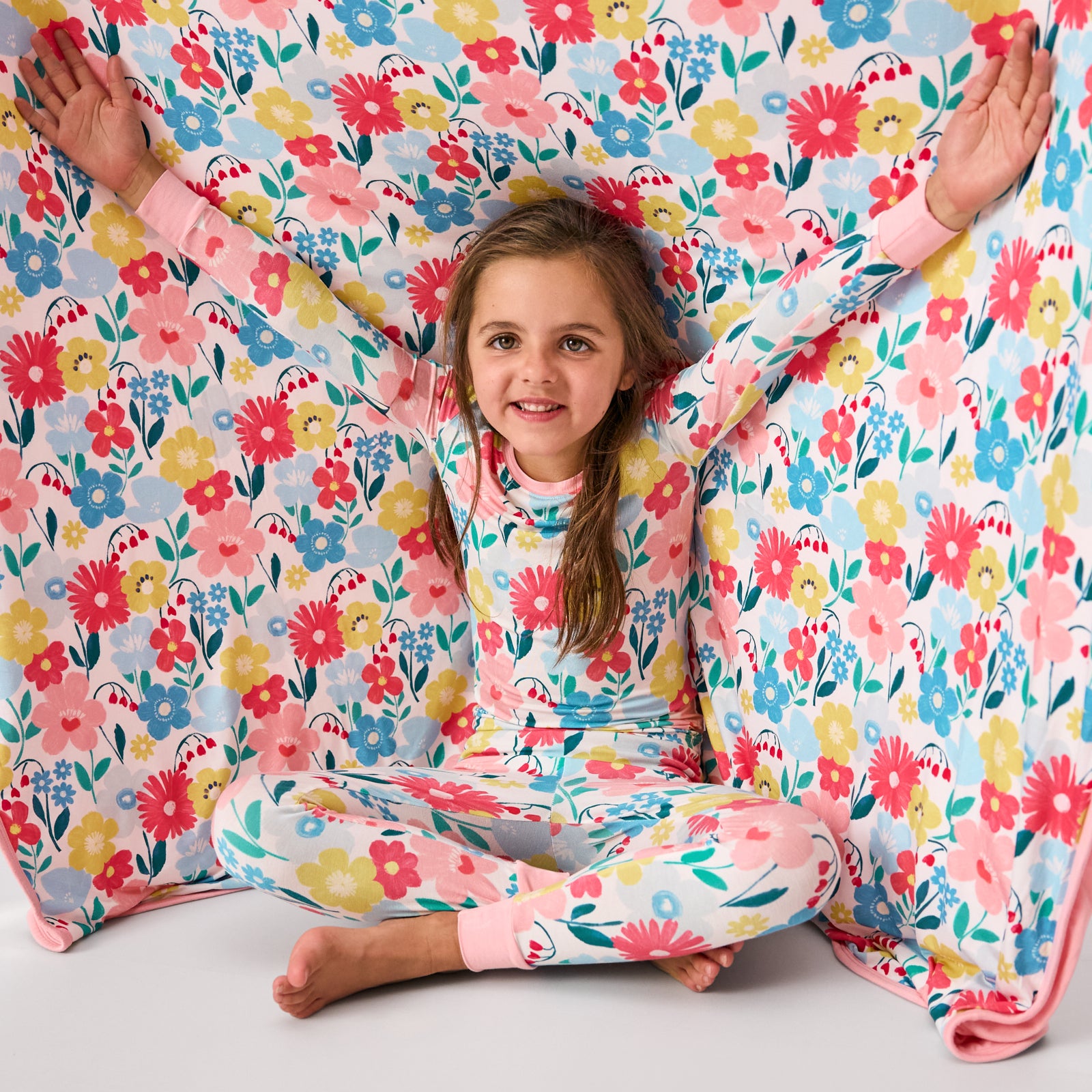 Sitting girl wearing the Midsummer Meadow PJs with the matching Large Cloud Blanket® as a back drop