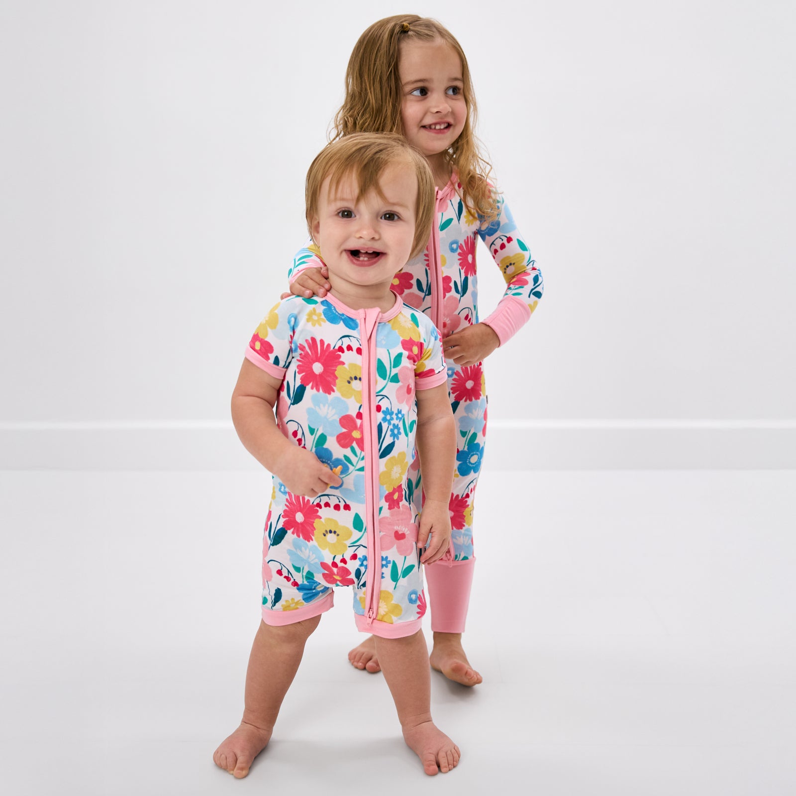 Two children wearing matching Midsummer Meadow floral zipper pajamas