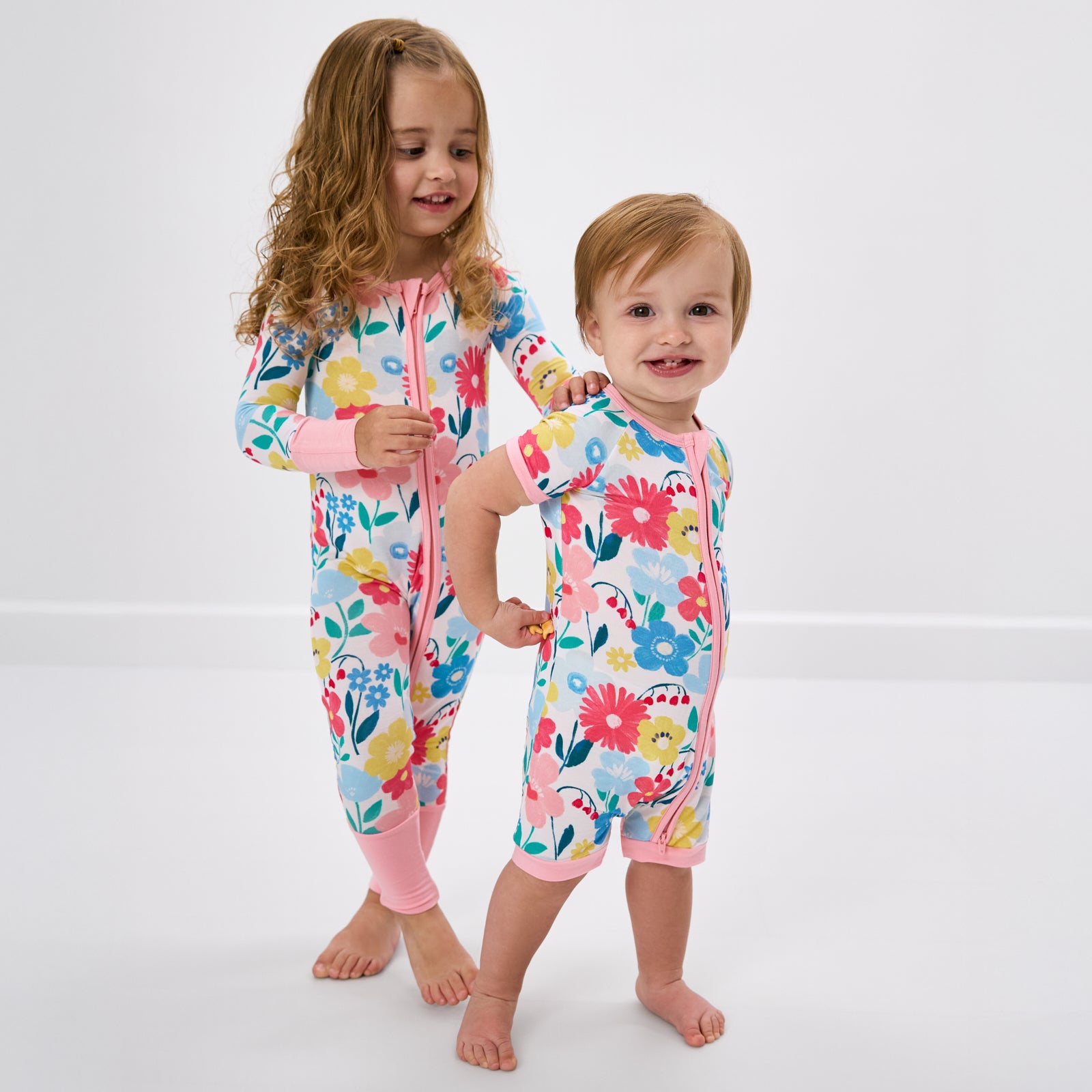 Two children wearing matching floral print pajamas on a white background