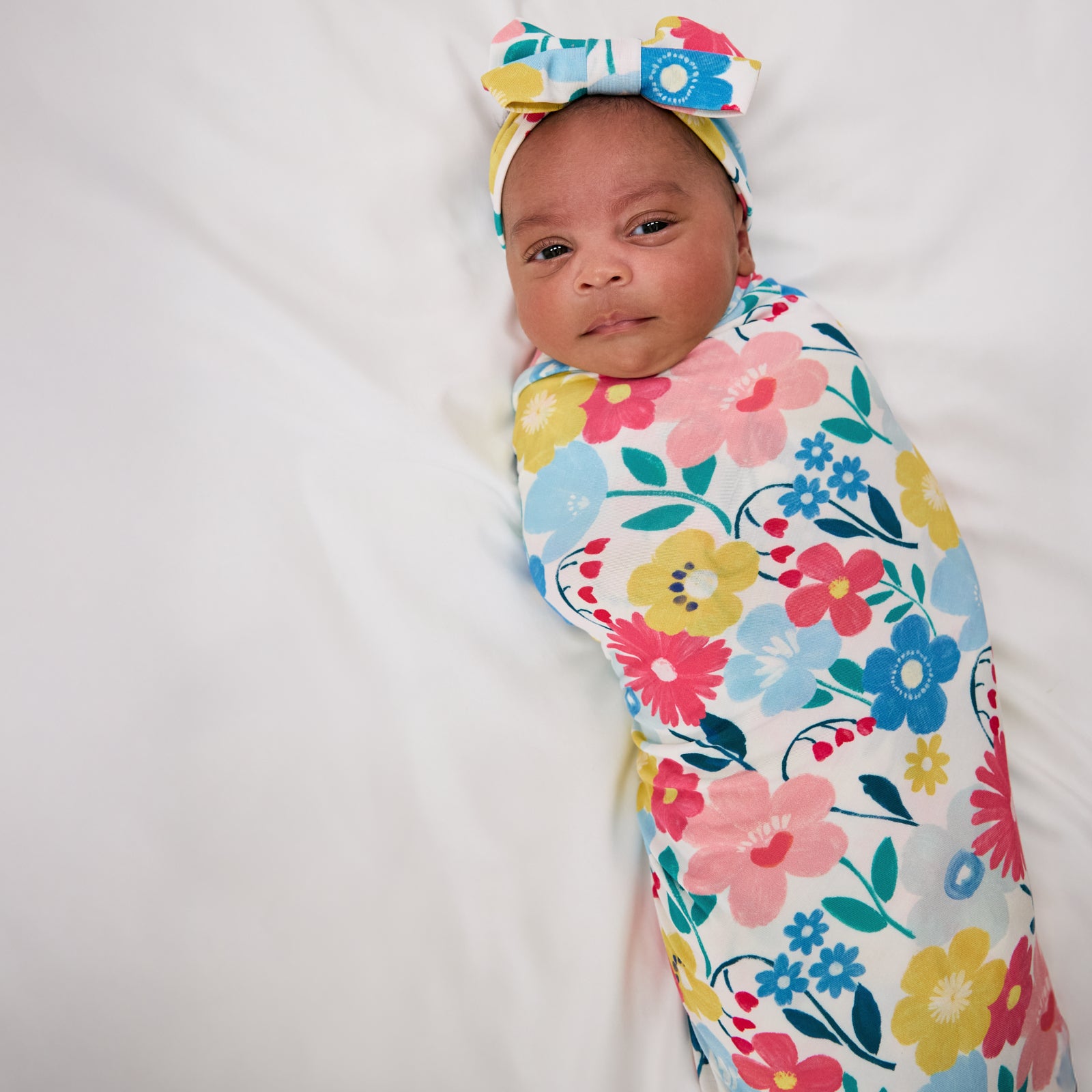 Aerial view of alternate baby wearing the Midsummer Meadow Swaddle & Luxe Bow Headband Set