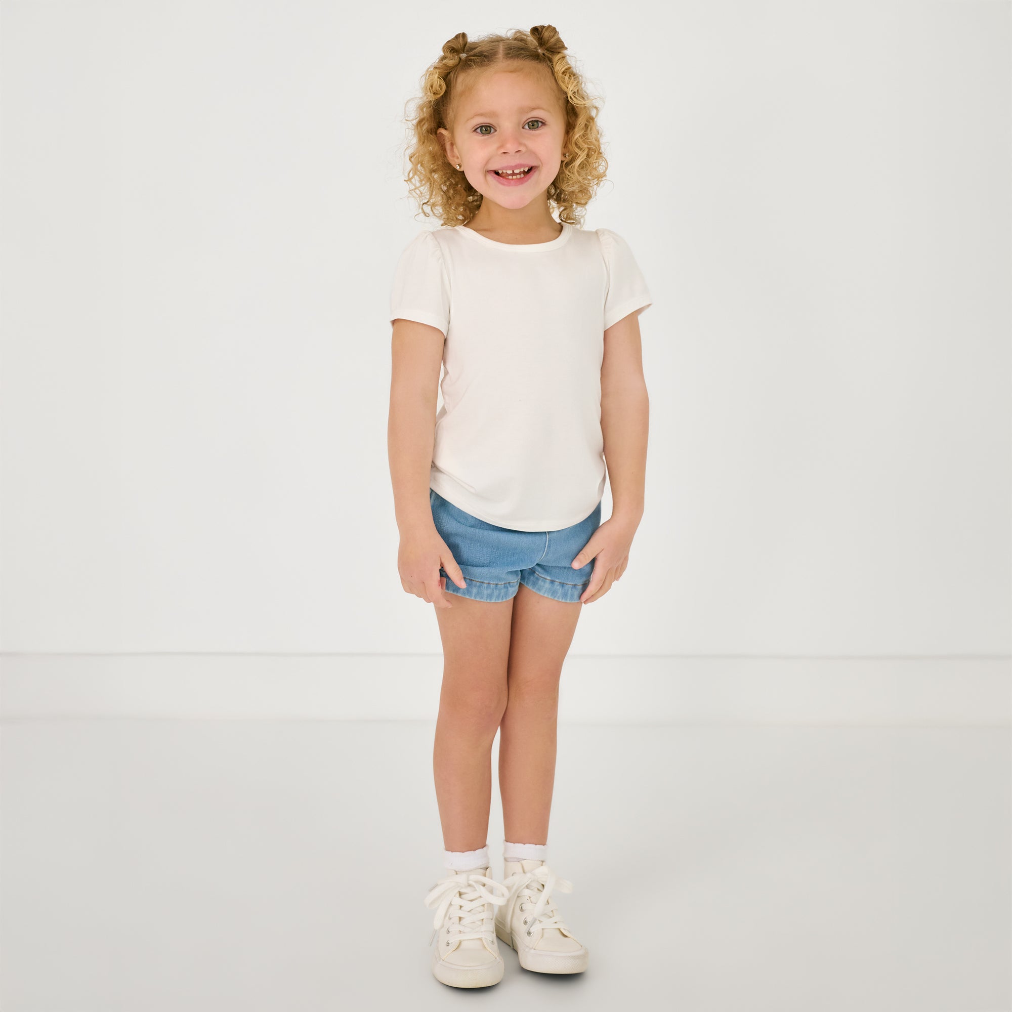 Standing child wearing the Midwash Blue Denim Shorts with a white puff sleeve tee
