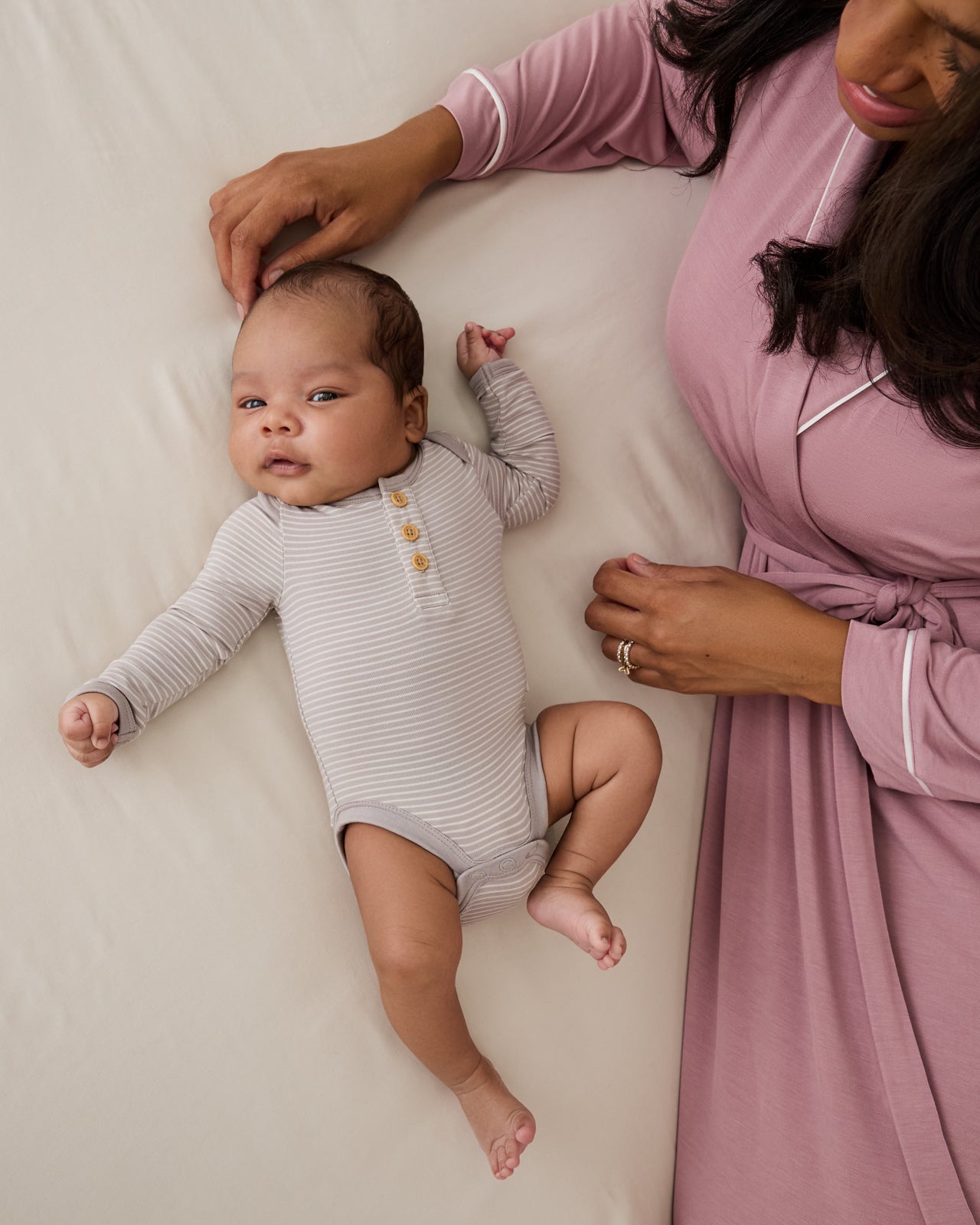 Mother and newborn on a bed wearing styles from the Newborn Capsule