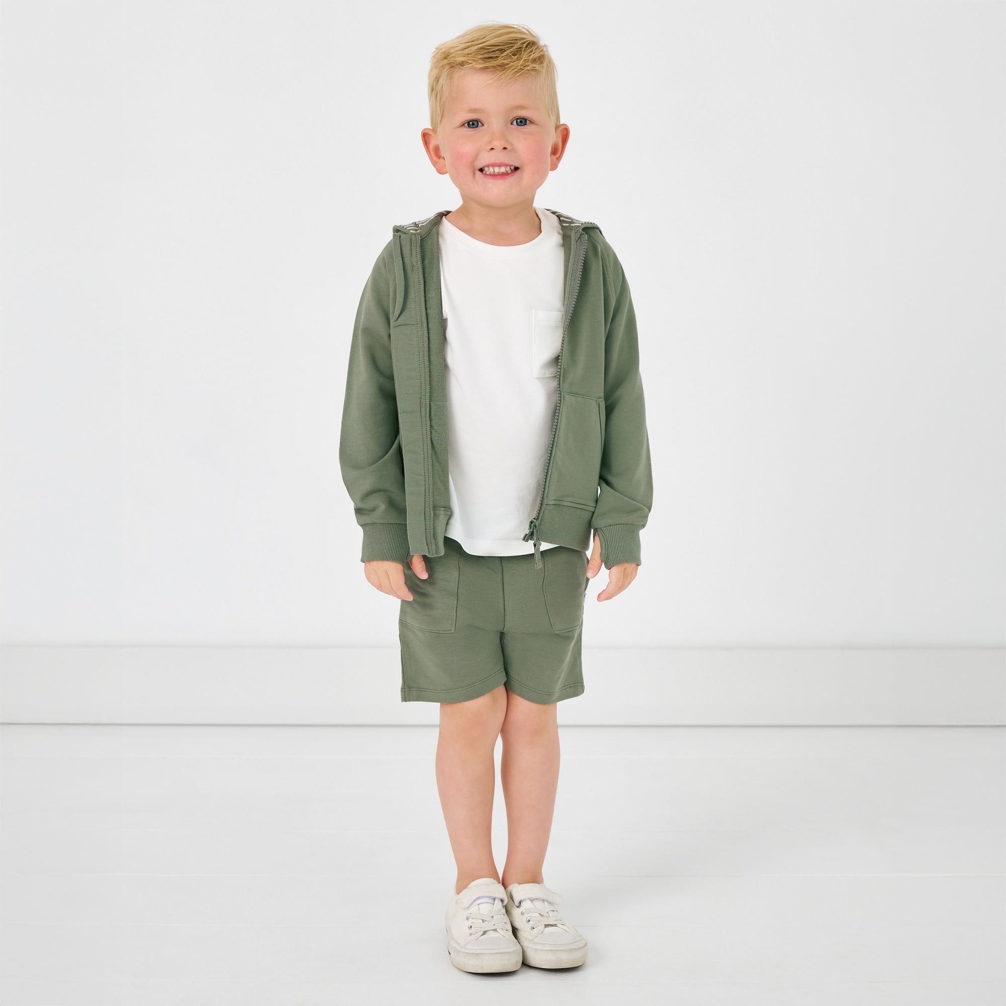 Standing child wearing the moss zip up hoodie and shorts