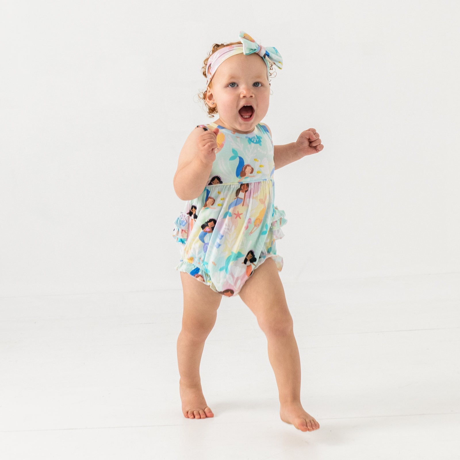 Walking child wearing the Mystic Mermaids Bubble Romper with a matching luxe bow headband