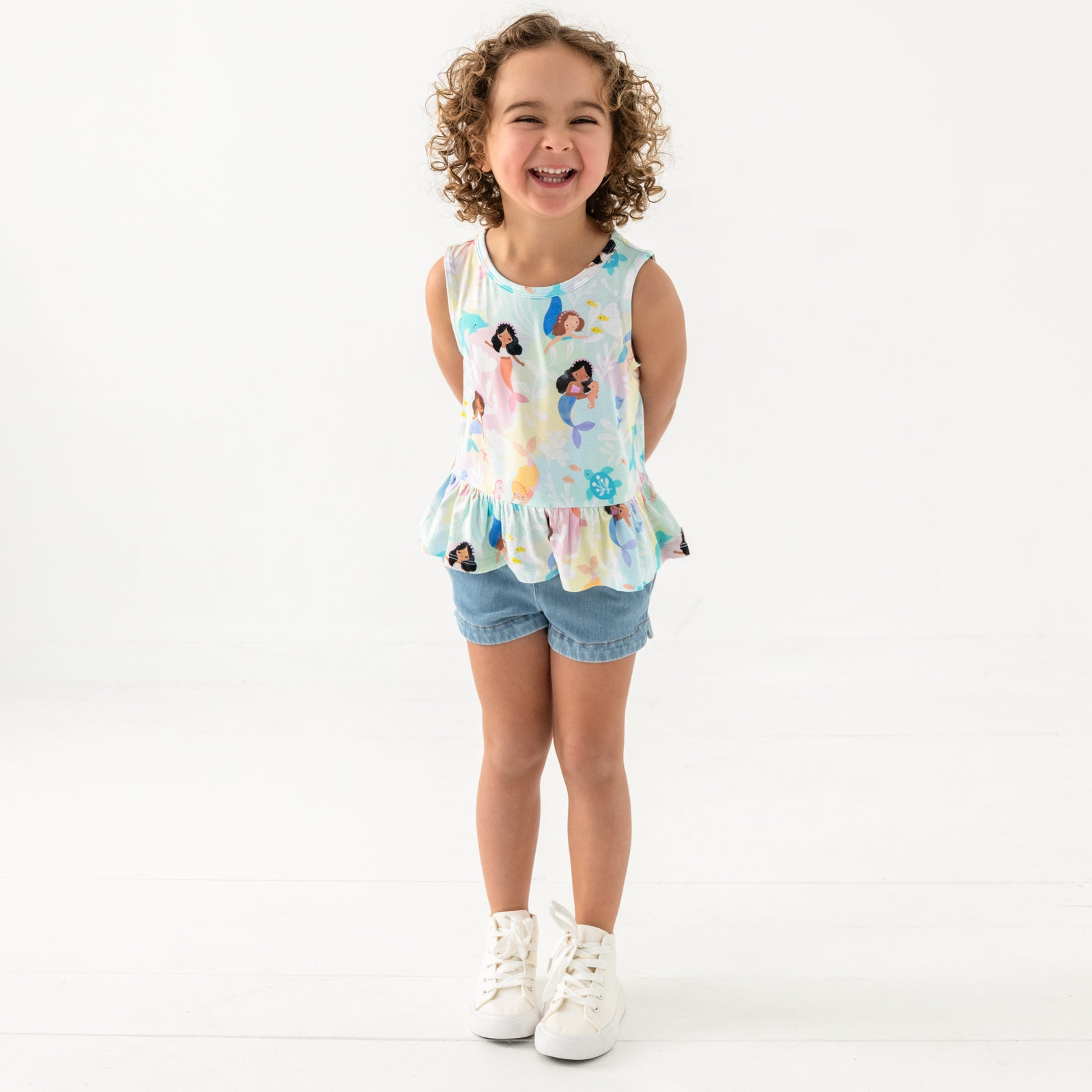 Standing child wearing the Mystic Mermaids Peplum Tank with blue denim shorts
