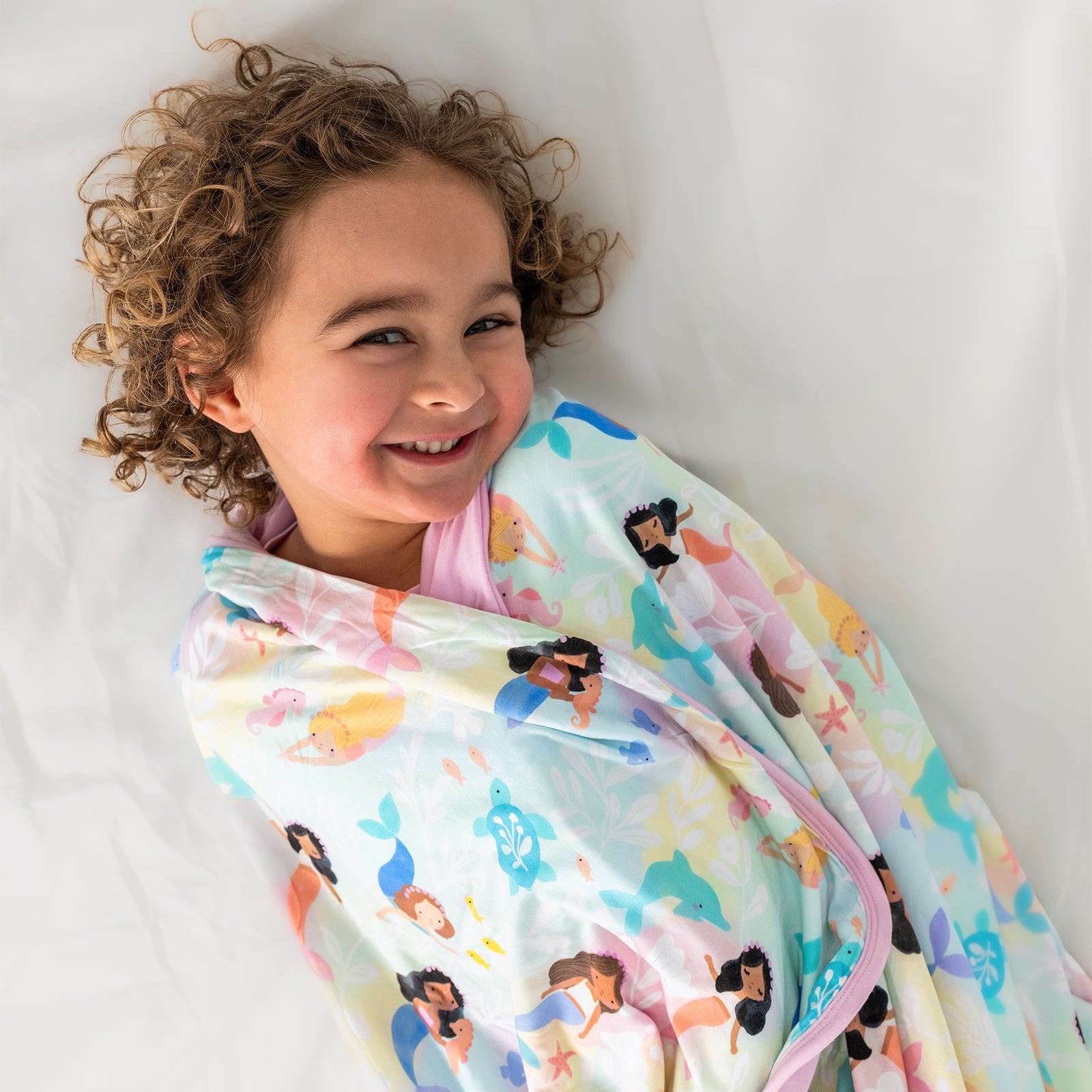 Aerial view of child wrapped in the Mystic Mermaids Large Cloud Blanket®