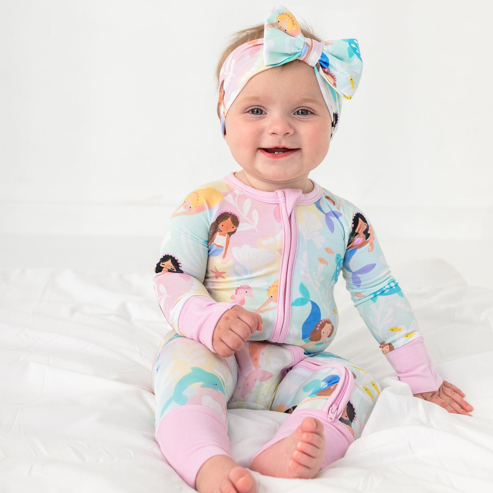 Sitting child wearing the Mystic Mermaids Luxe Bow Headband and matching bamboo zipper pajamas