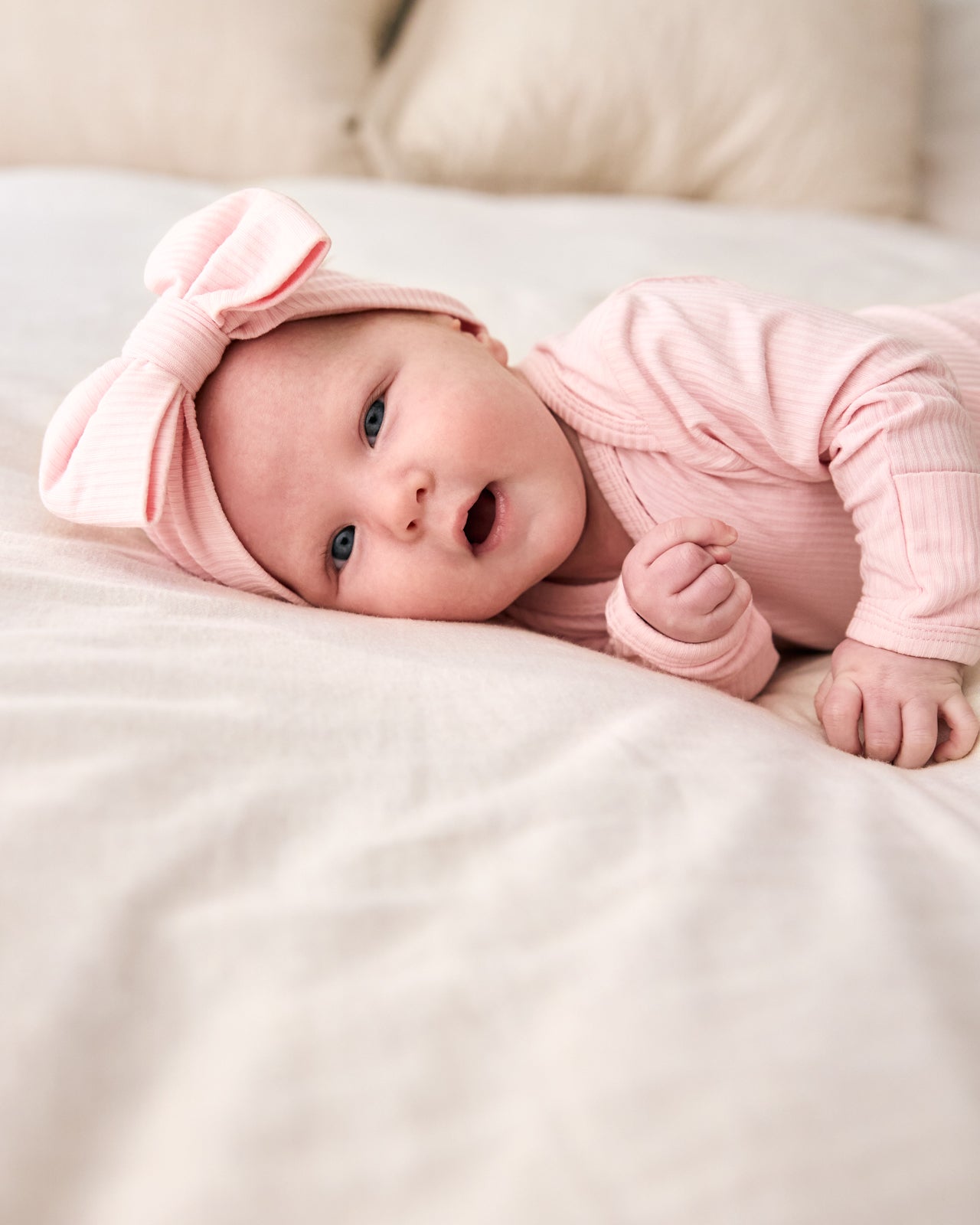 Newborn on a white bed wearing the Prima Pink Ribbed Luxe Bow Headband
