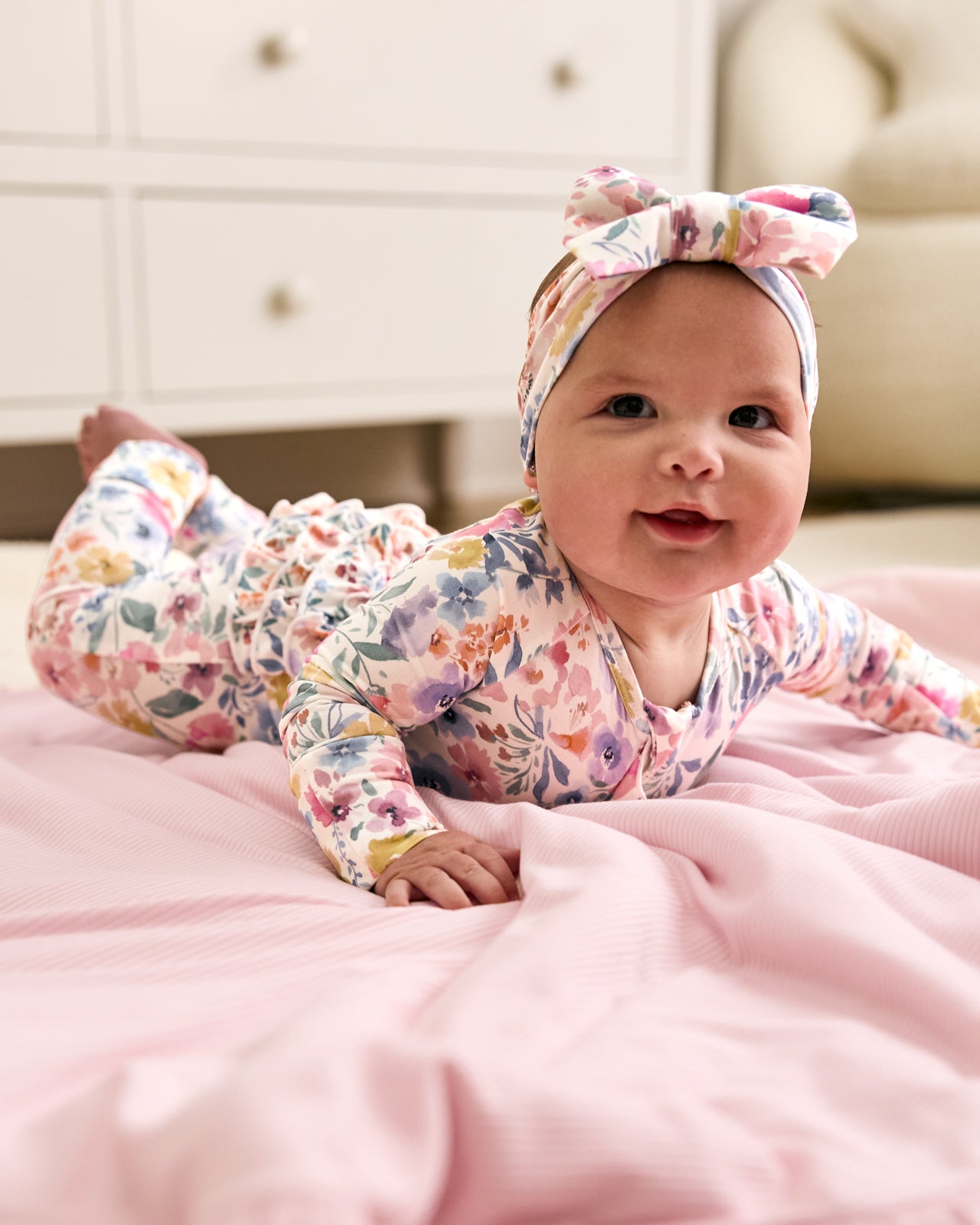 Newborn laying on a pink baby blanket wearing the Tiny Blooms Ruffle Zippy
