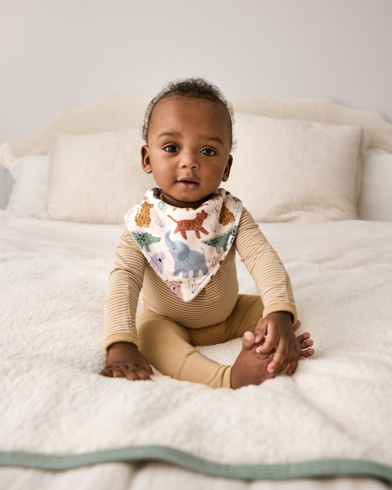 Newborn sitting on the bed wearing the Sweet Safari Bandana Bib