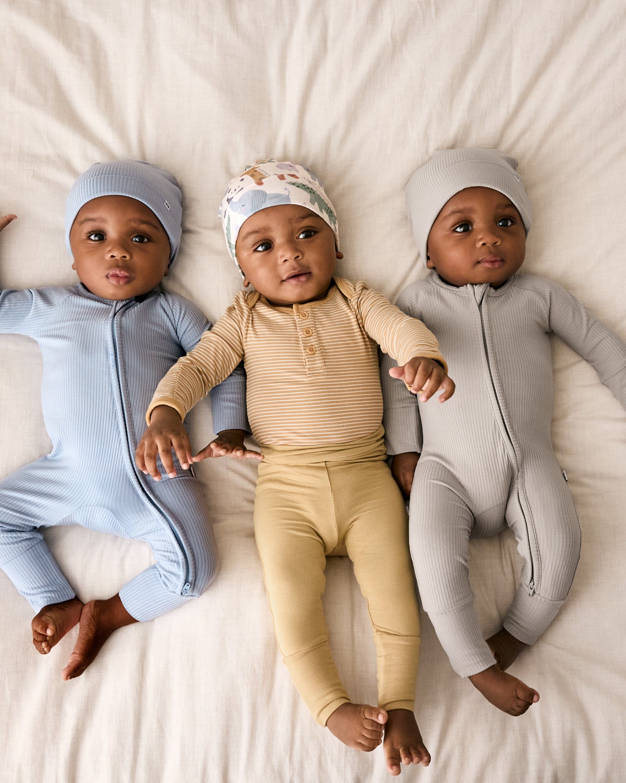 Aerial view of three babies wearing styles from the Newborn Capsule