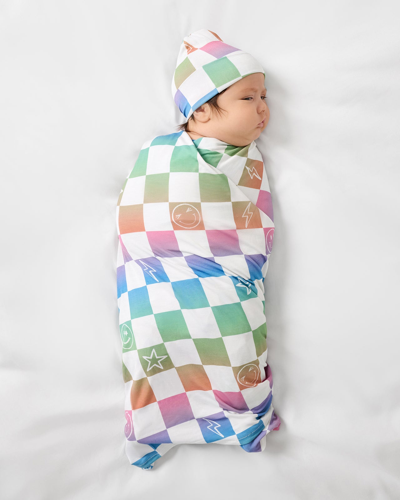 Aerial view of baby wearing the Ombre Cheery Checks Swaddle & Hat Set
