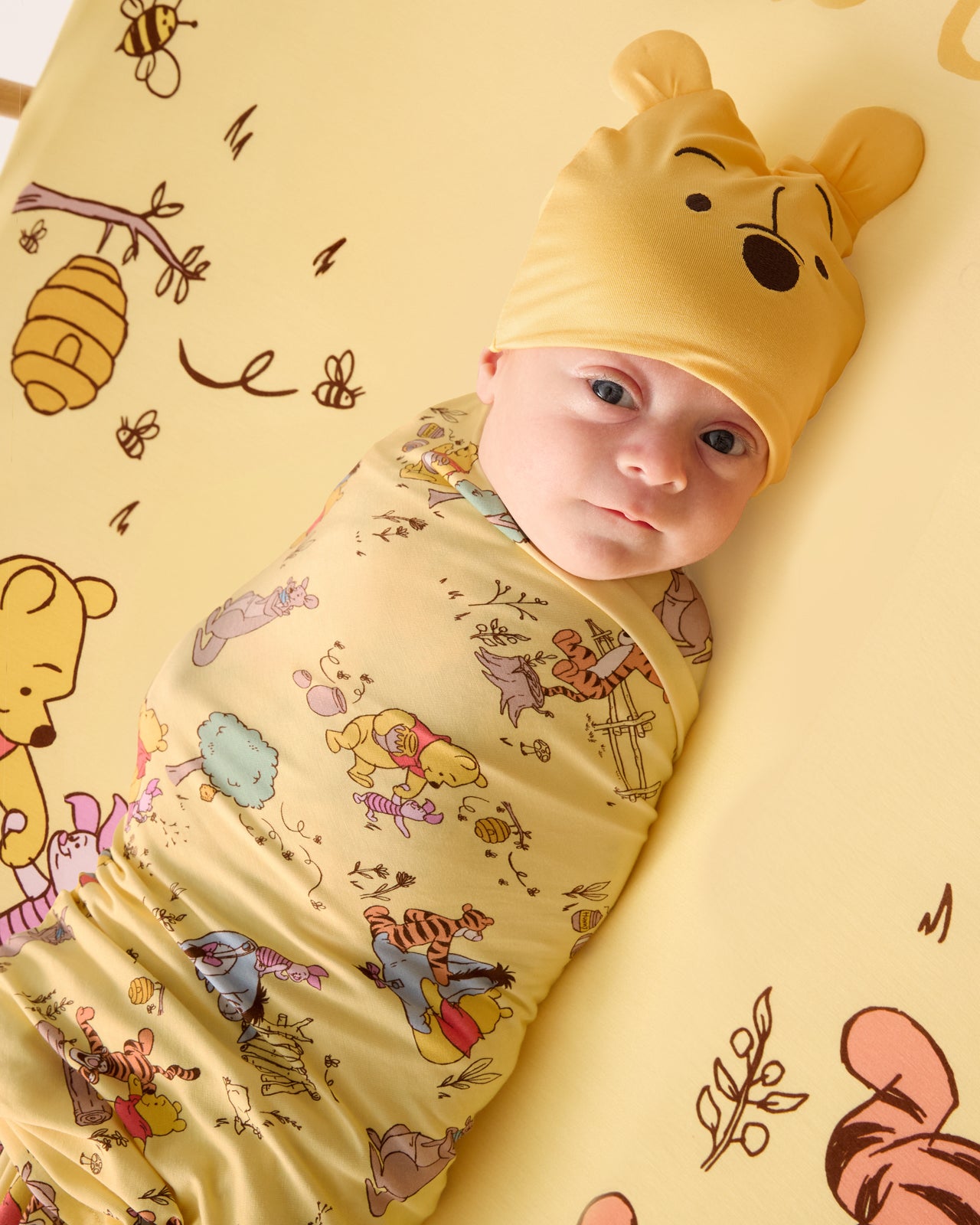 Aerial view of abby wearing the Disney Playtime With Pooh Swaddle & Hat Set in a crib