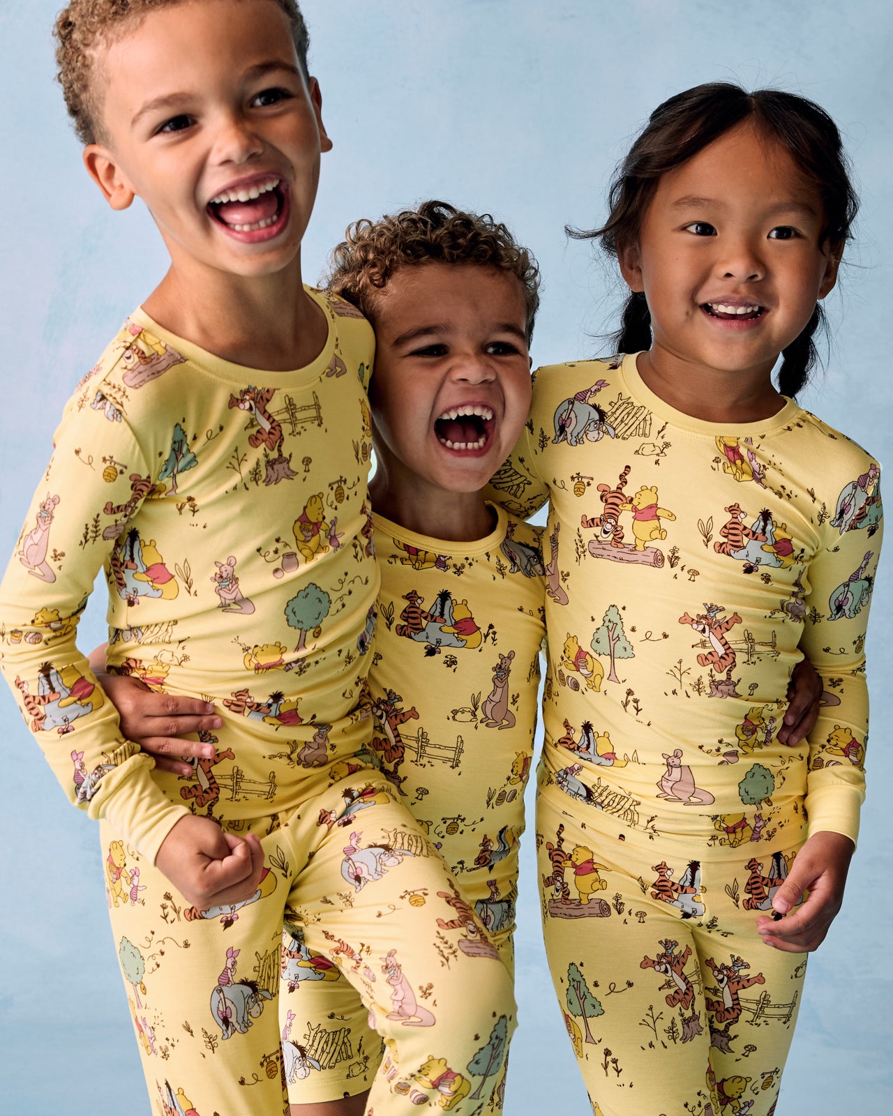 Three children wearing Disney Playtime With Pooh Two-Piece Pajama Sets on a blue background