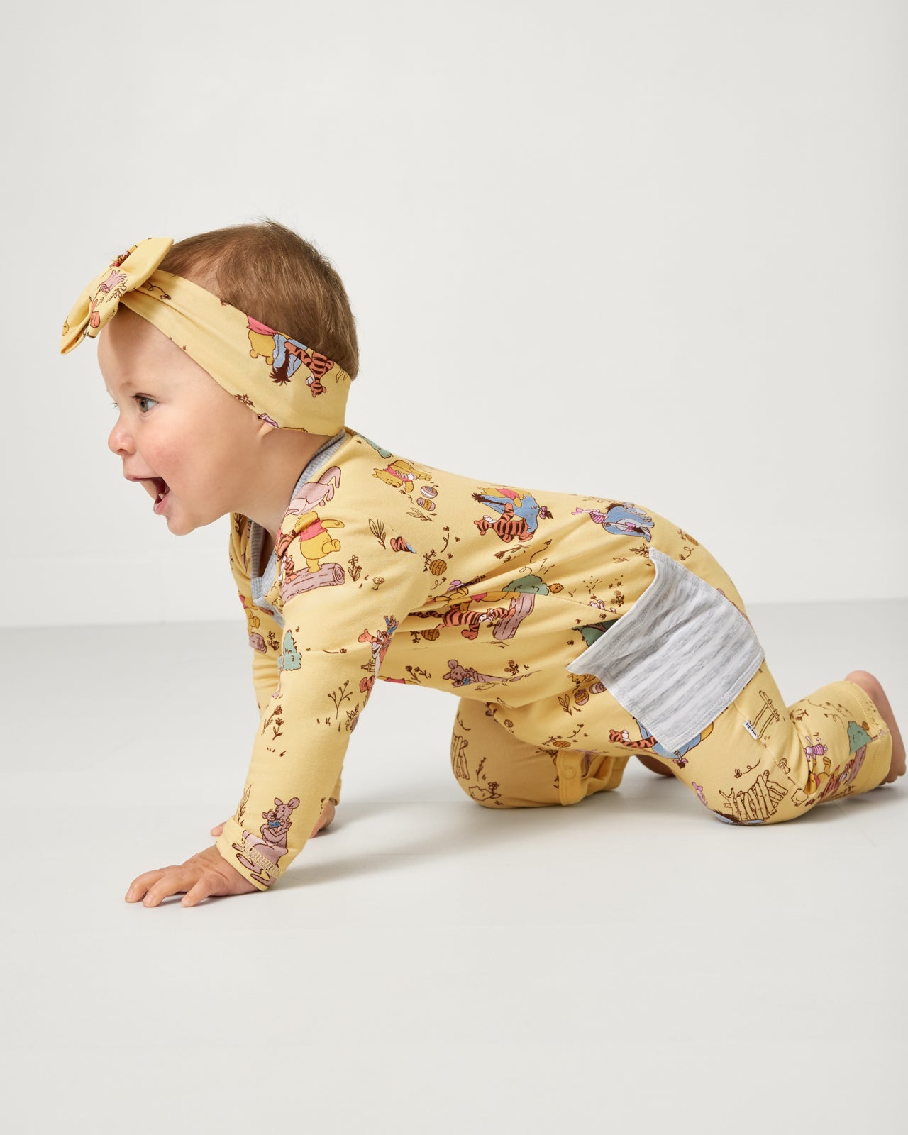 Crawling child wearing the Disney Playtime With Pooh Henley Romper with a luxe bow headband