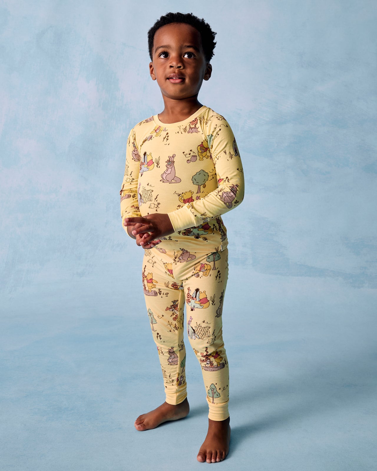Standing boy wearing the Disney Playtime With Pooh Two-Piece Pajama Set on a blue background
