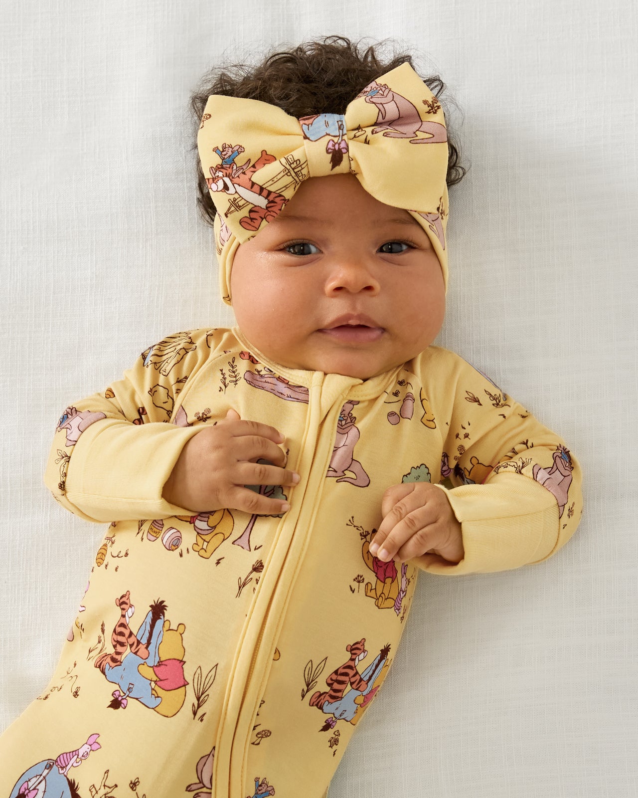 Close up of baby wearing the Disney Playtime With Pooh Zippy with a matching bow headband