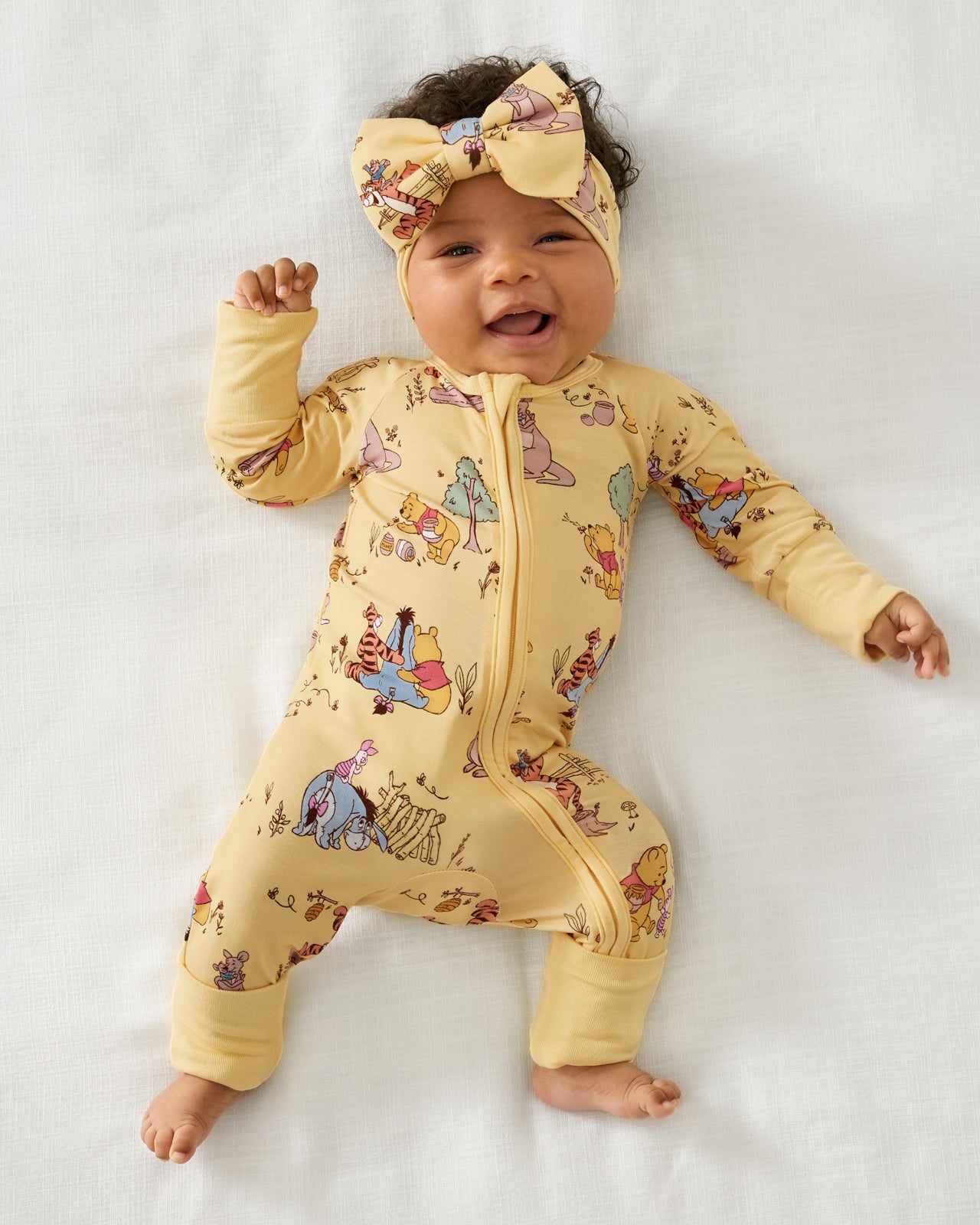 Alternate aerial view of baby wearing the Disney Playtime With Pooh Zippy and matching bow headband