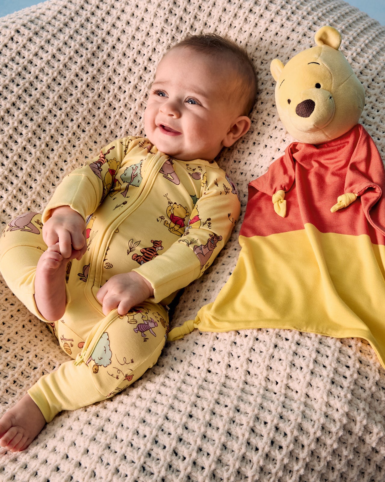 Baby laying with the Disney Winnie The Pooh Lovey on a knit blanket